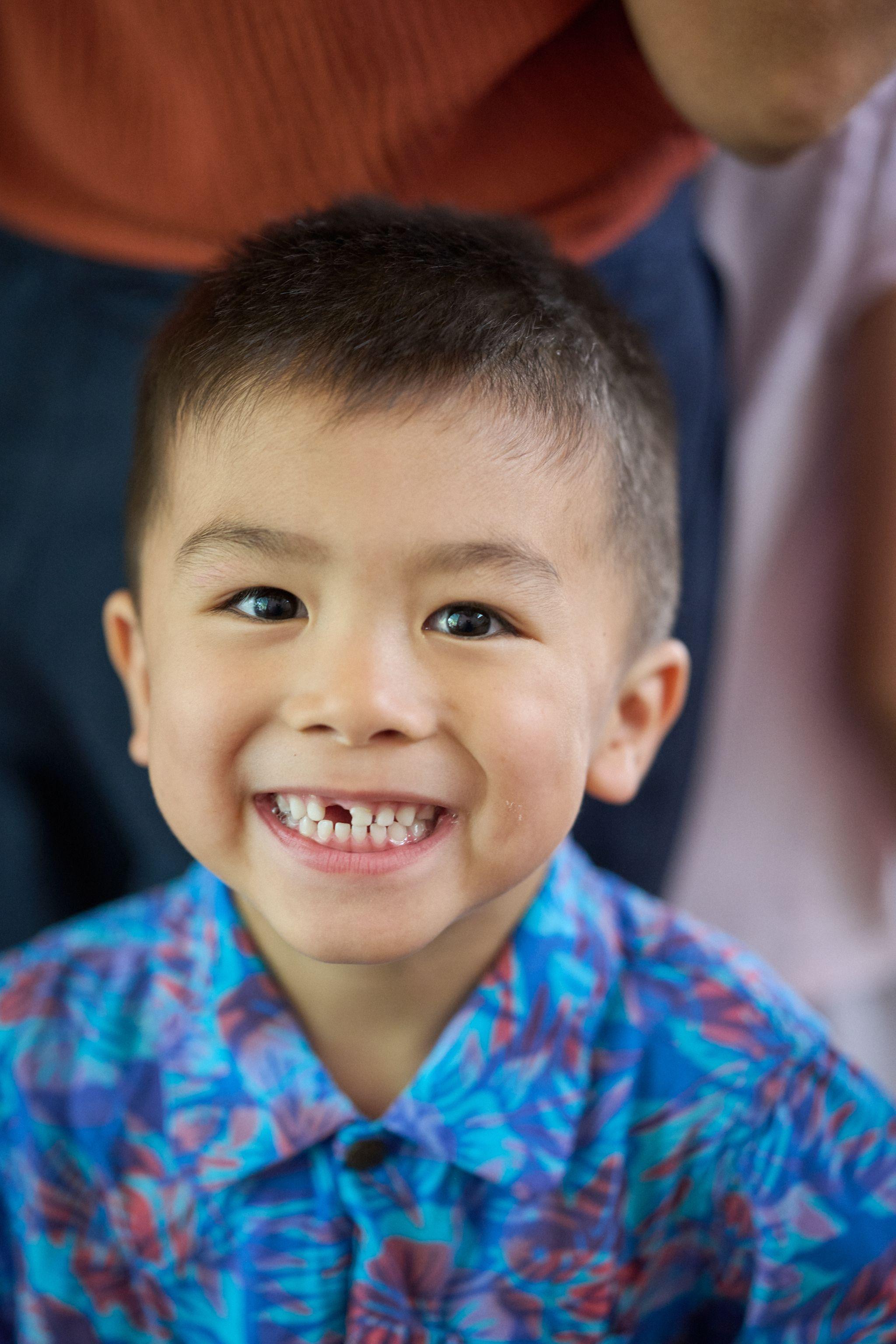 Boy in a bright blue floral shirt grinning at camera, missing a front tooth — Kids Portraits photography, Austin A boy in a bright blue floral shirt grinning at camera, missing a front tooth.