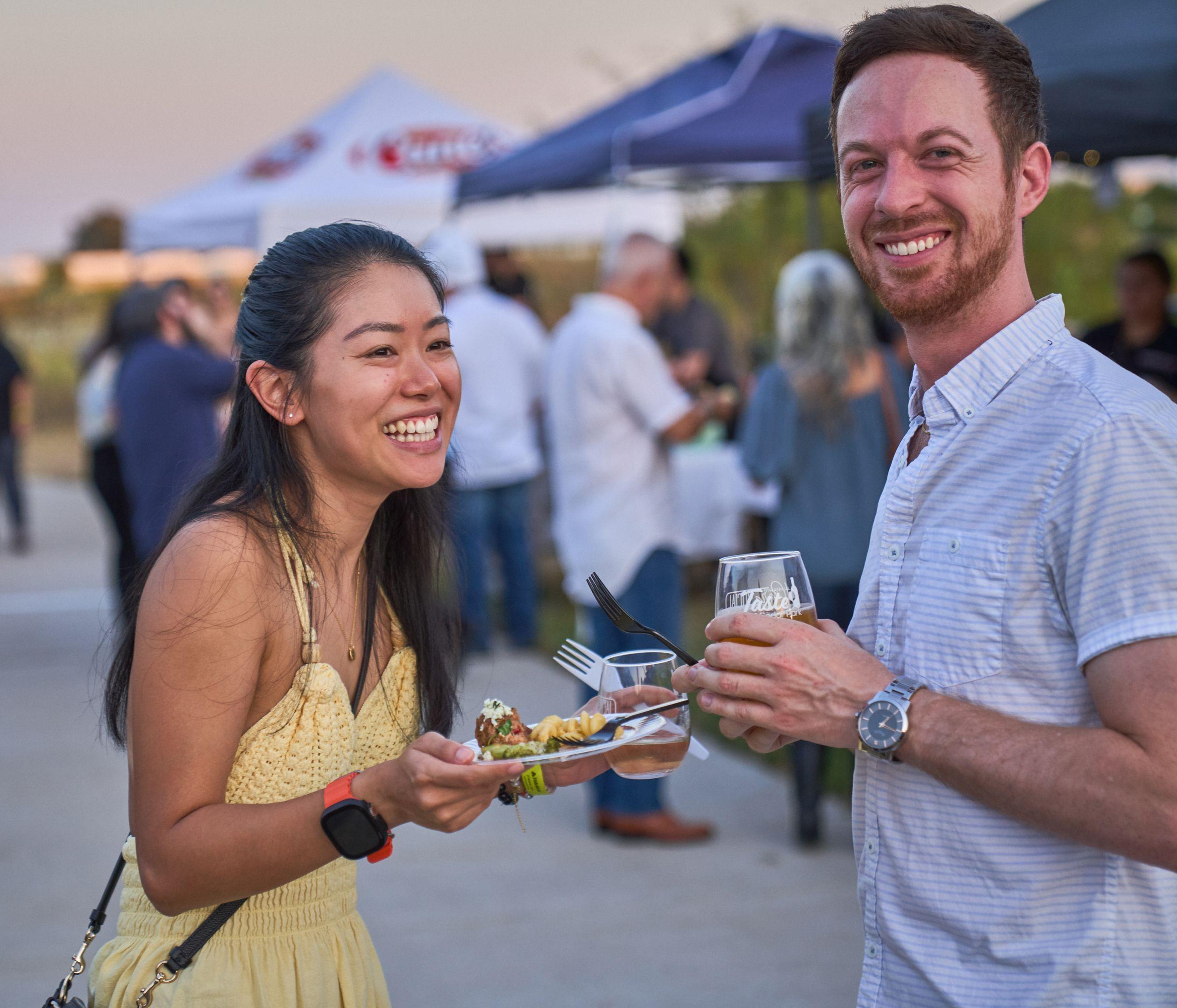 Two festival-goers smiling with tasting plates and wine glasses — Festival photography, Austin Two festival-goers smiling with tasting plates and wine glasses.