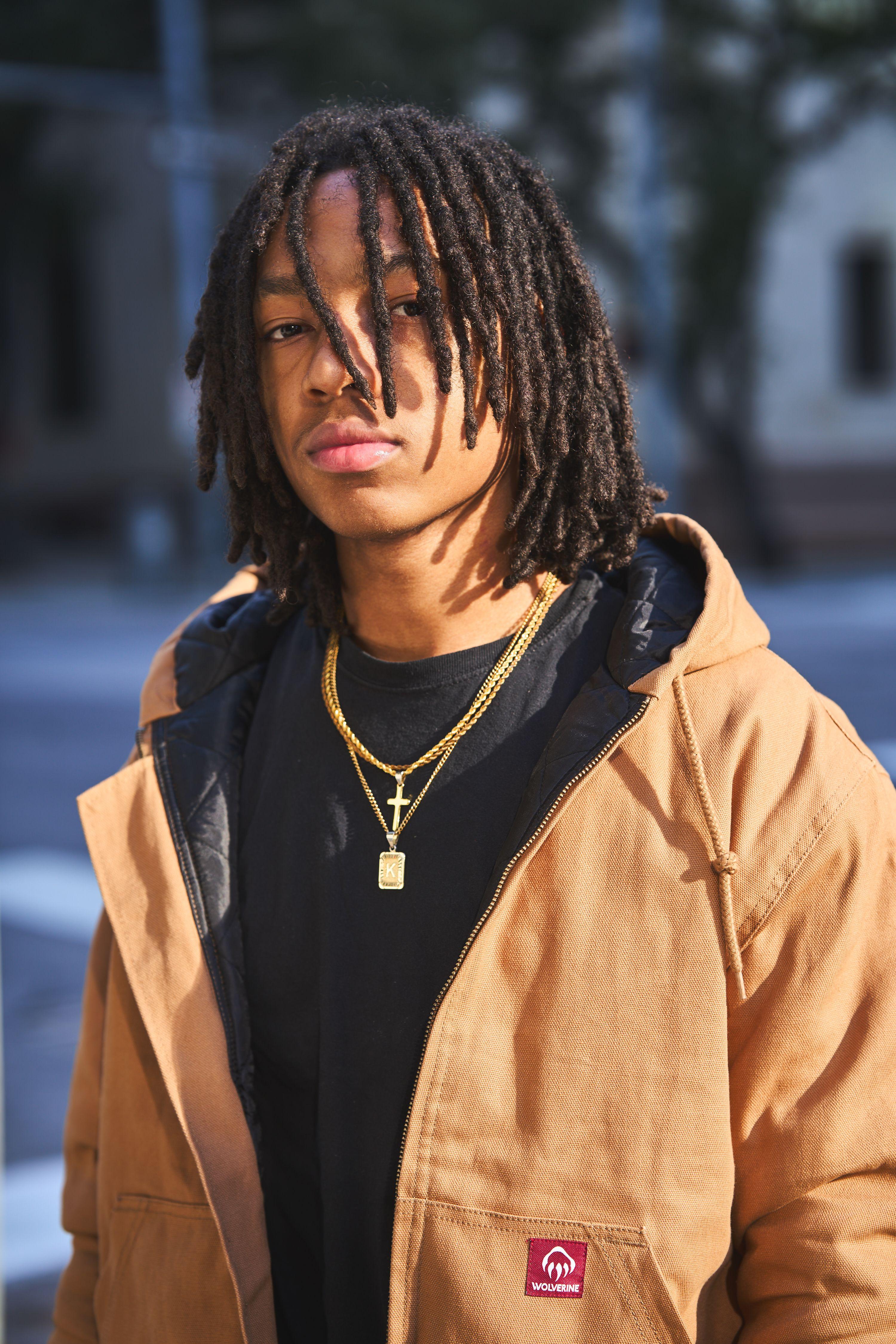 Model in a tan hooded work jacket over a black hoodie and gold chain, standing — E-commerce & apparel photography, Austin Model in a tan hooded work jacket over a black hoodie and gold chain, standing on a downtown street