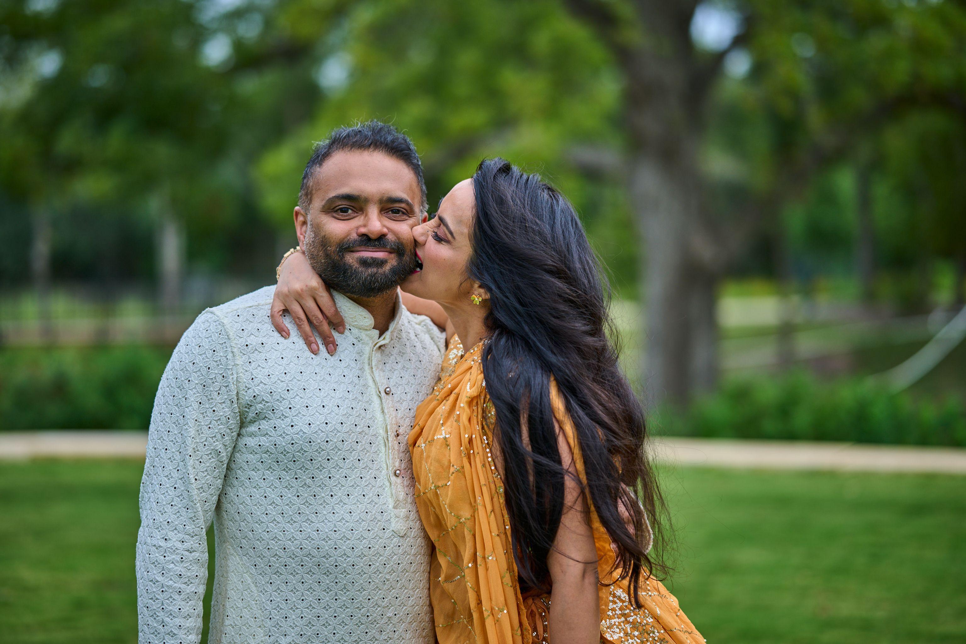 Woman in a gold sari kissing her husband's cheek at an outdoor family celebration — Cedar Park Public Library photography, Austin A woman in a gold sari kissing her husband's cheek at an outdoor family celebration.