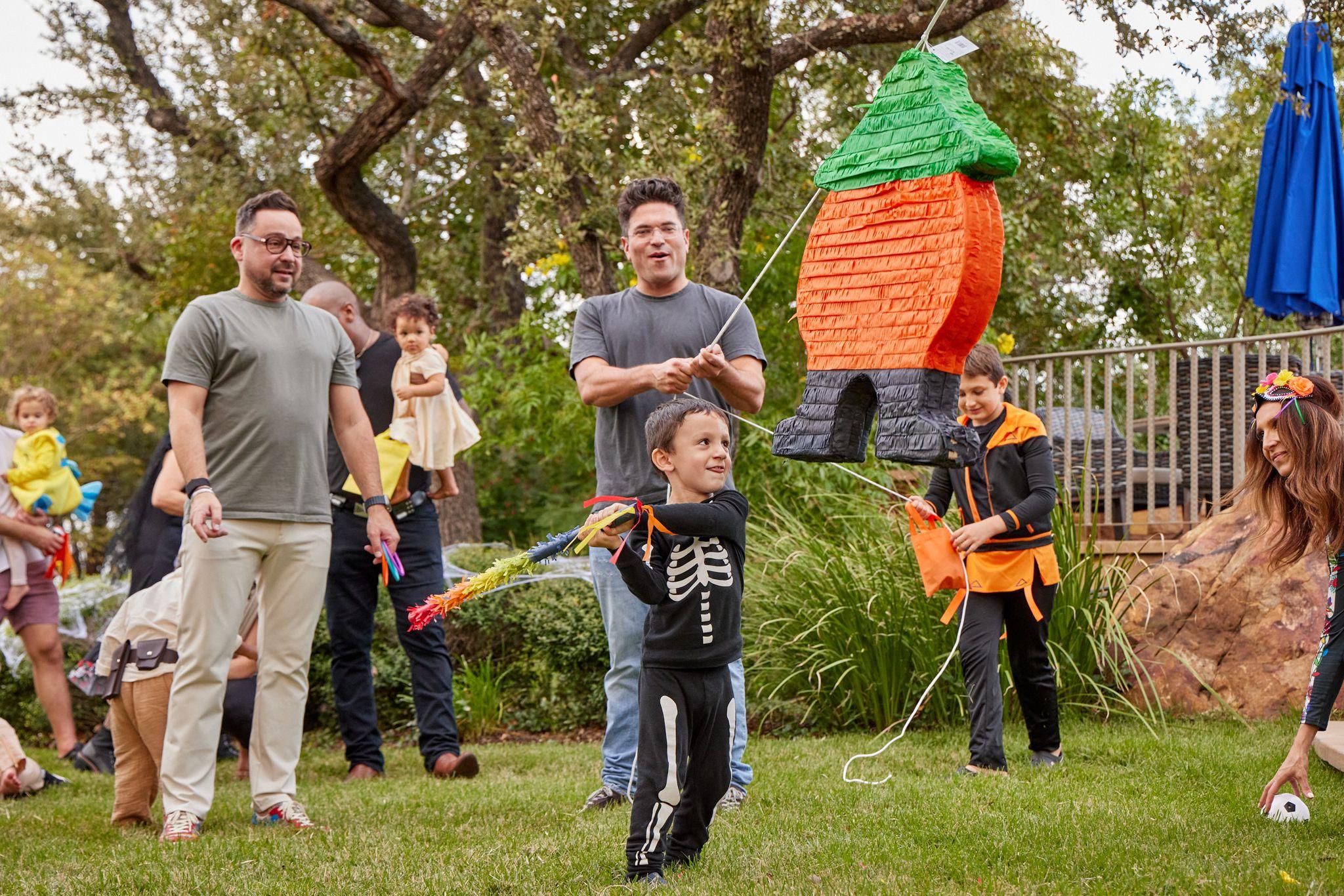Boy in a skeleton costume swinging a stick at a piñata on a lawn — Family Parties photography, Austin A boy in a skeleton costume swinging a stick at a piñata on a lawn.