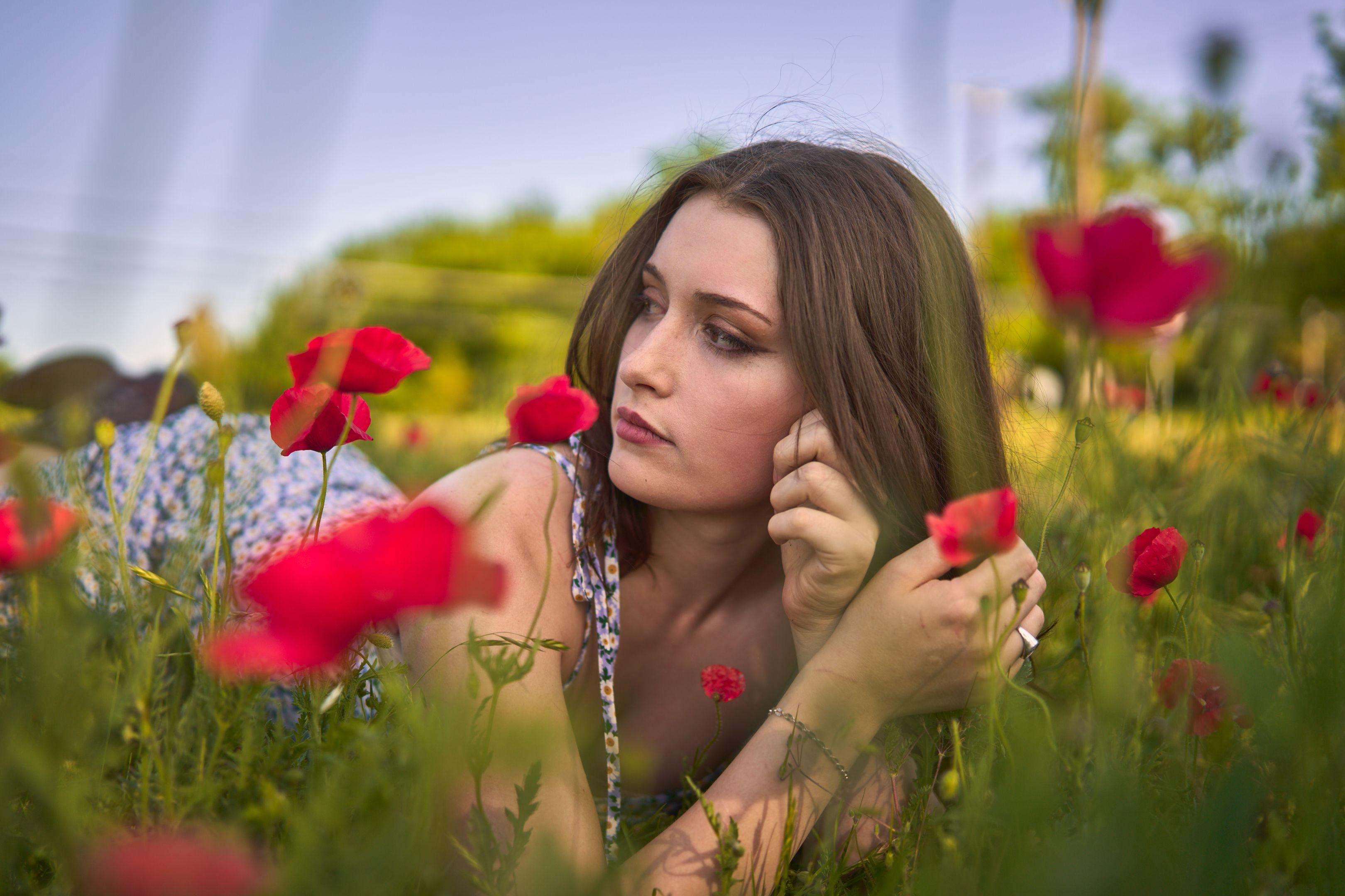 A woman in a floral dress lying in a field of red poppies with one hand in her hair