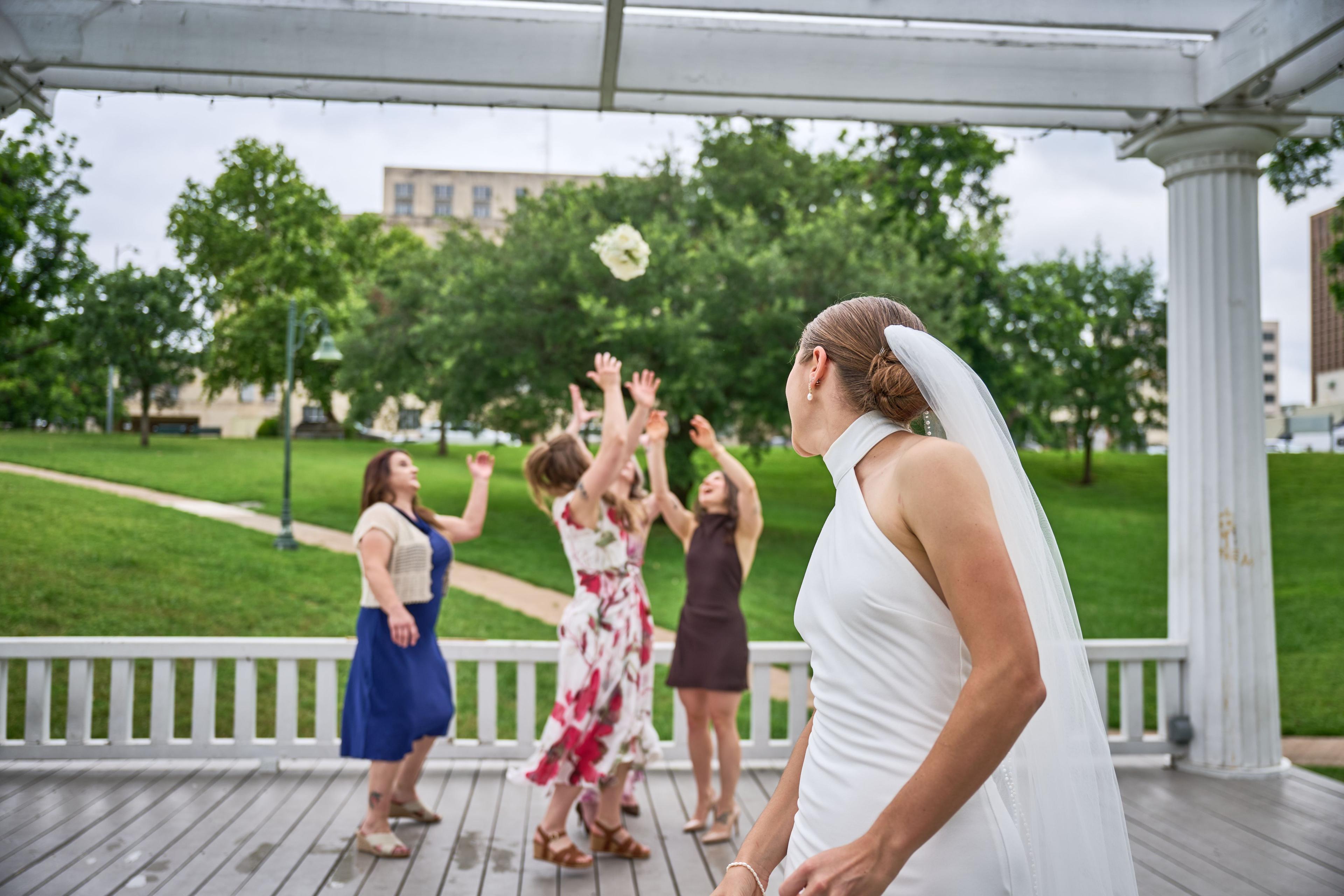 Guests reaching for the bouquet as the bride throws it across a green lawn — Weddings photography, Austin Guests reaching for the bouquet as the bride throws it across a green lawn.