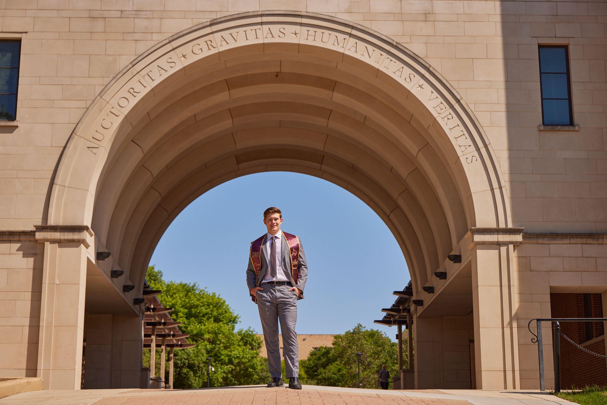 Graduate standing inside the stone arch at Texas State University, the campus falling away — Texas State University photography, Austin A graduate standing inside the stone arch at Texas State University, the campus falling away behind him