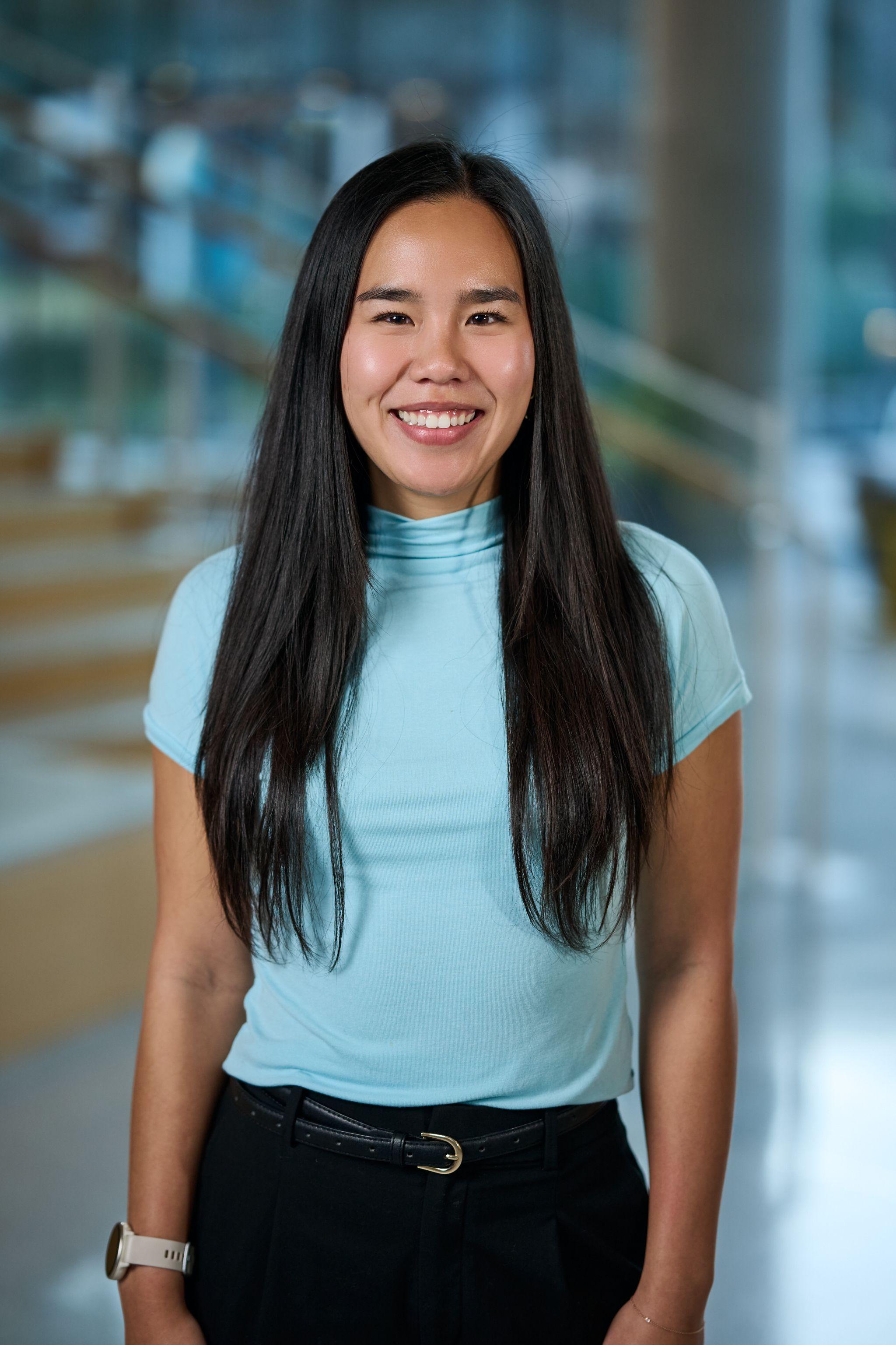 Woman with long dark hair in a pale turquoise top, photographed — Business headshots, Austin A woman with long dark hair in a pale turquoise top, photographed against a bright office interior