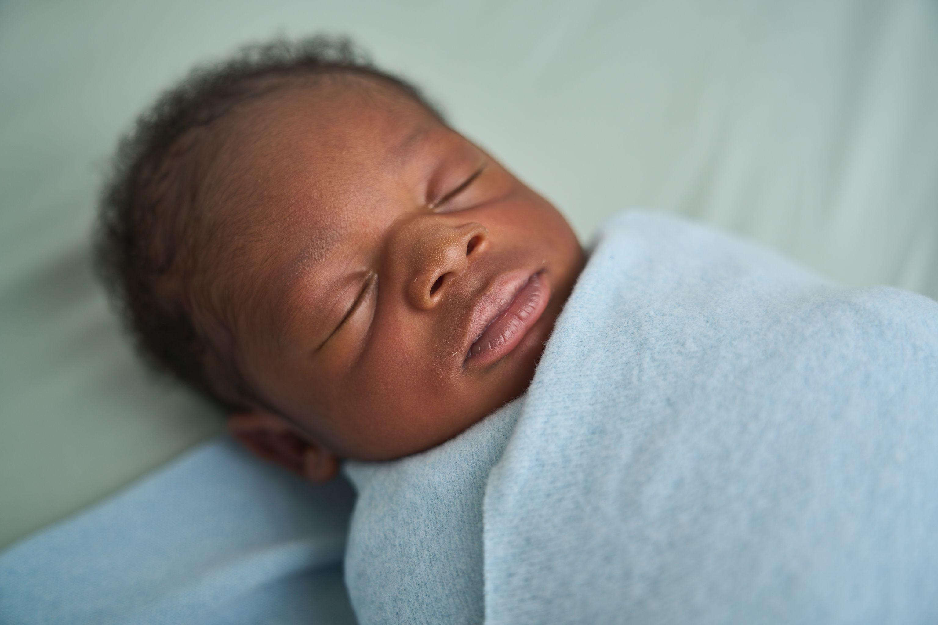 Close portrait of a sleeping newborn wrapped in a blue swaddle — Newborn photography, Austin A close portrait of a sleeping newborn wrapped in a blue swaddle.