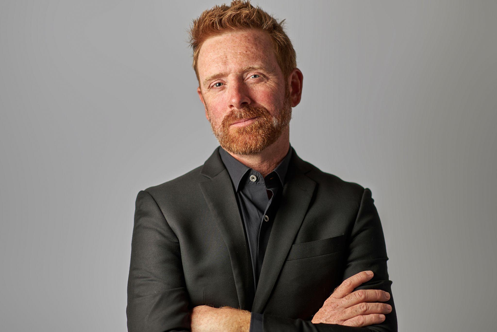 Red-haired man in a black jacket standing with arms crossed outdoors — Headshot photography, Austin A red-haired man in a black jacket standing with arms crossed outdoors.