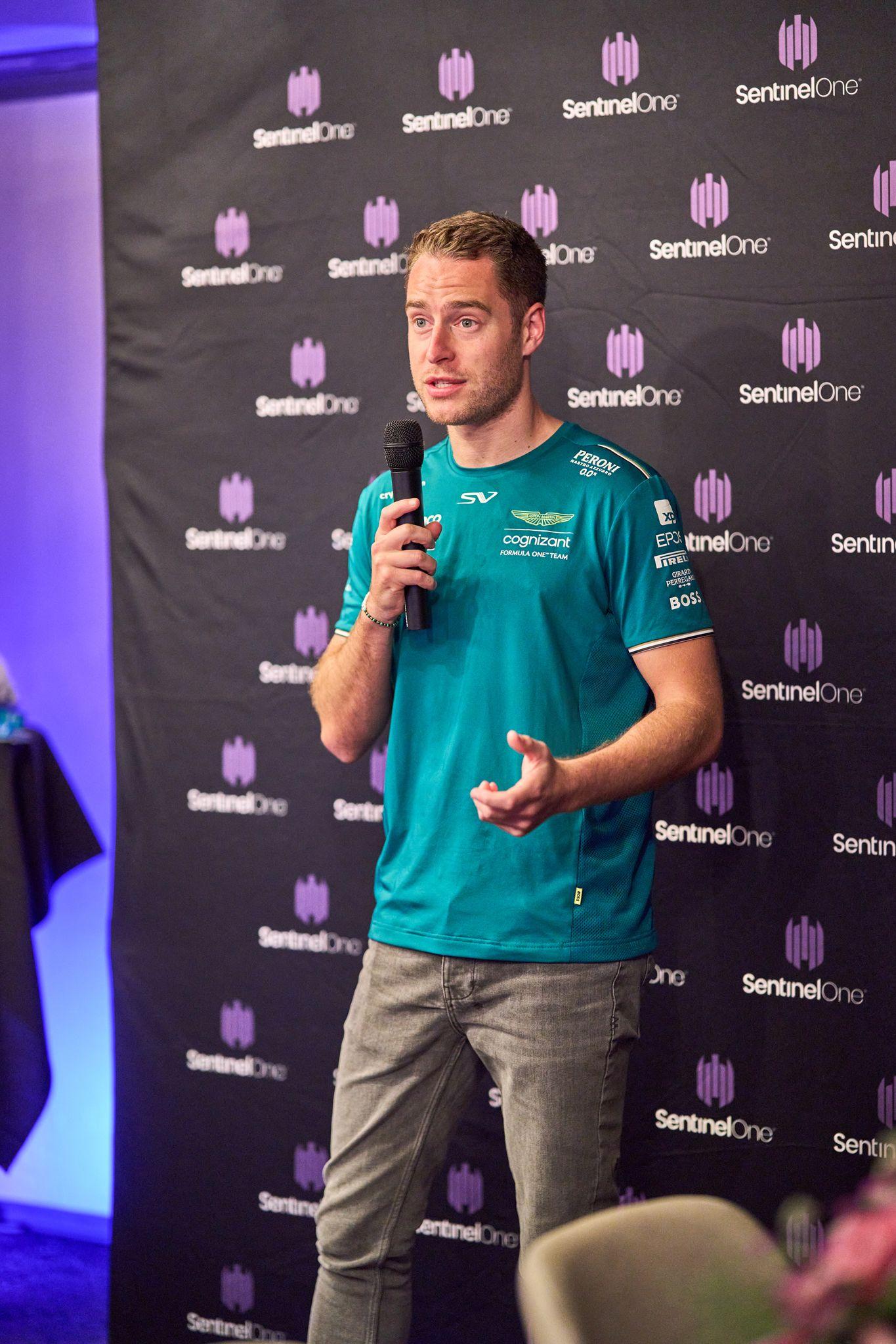 Aston Martin Formula 1 driver in team green speaking into a handheld microphone — Brand Collaborations photography, Austin An Aston Martin Formula 1 driver in team green speaking into a handheld microphone against a SentinelOne backdrop.