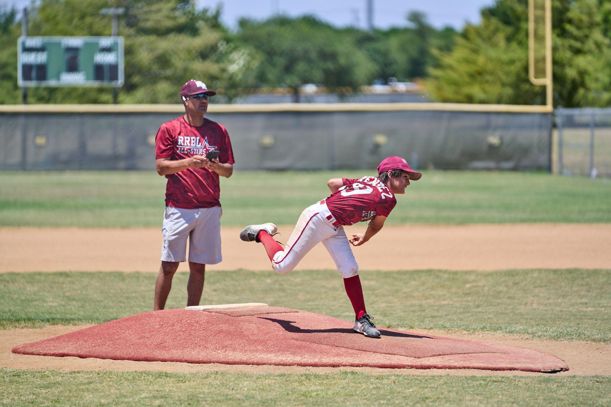 Baseball pitcher mid-delivery off the mound with a coach watching — Sports photography, Austin Baseball pitcher mid-delivery off the mound with a coach watching from behind