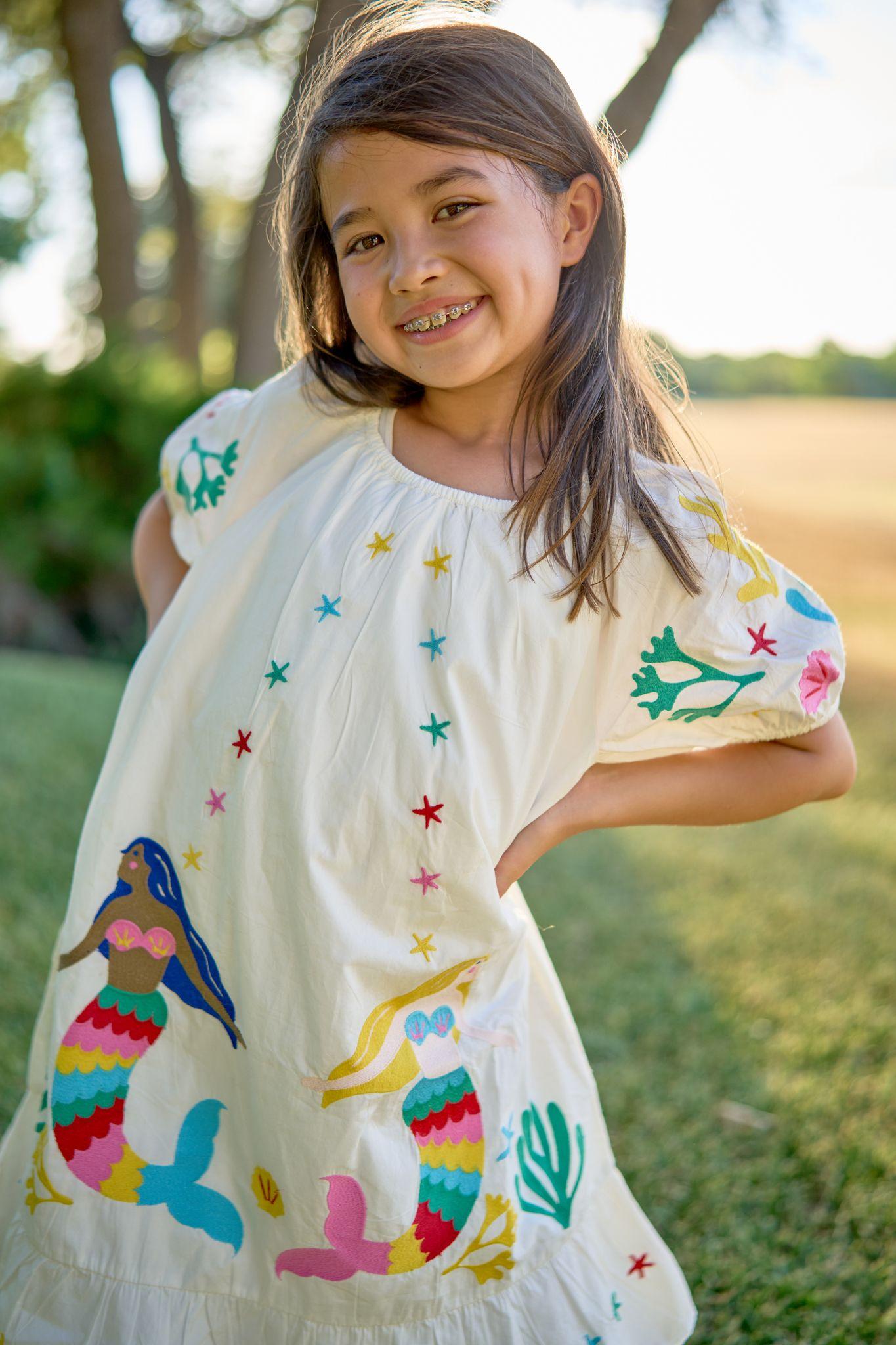 Girl in a brightly embroidered white dress turning to camera in a field — Kids Portraits photography, Austin A girl in a brightly embroidered white dress turning to camera in a field.