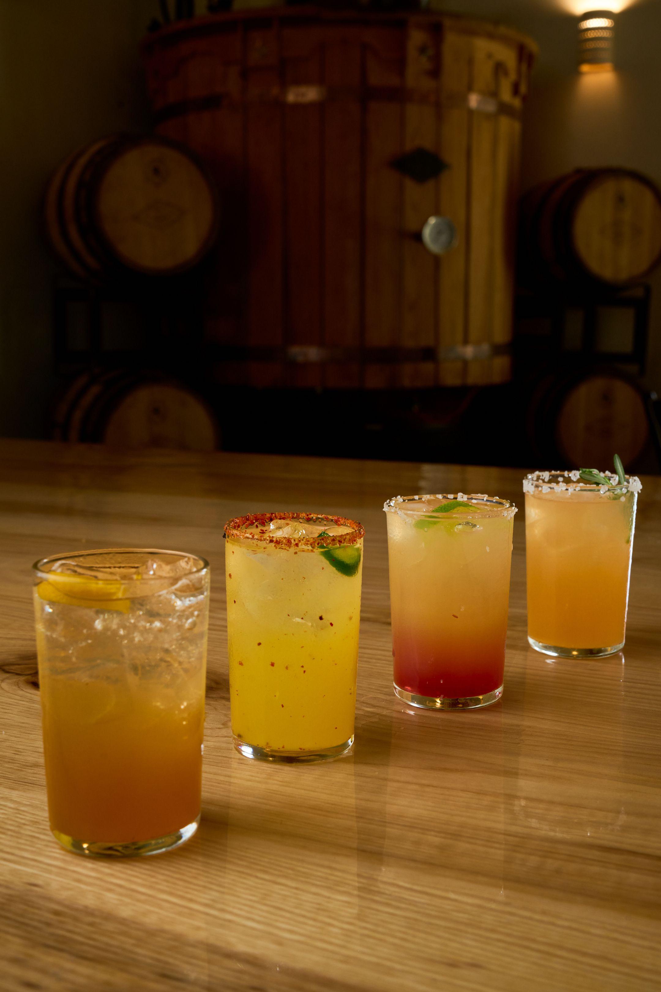 Four cocktails in different colors lined up along a wooden bar — Food & restaurant photography, Austin Four cocktails in different colors lined up along a wooden bar.