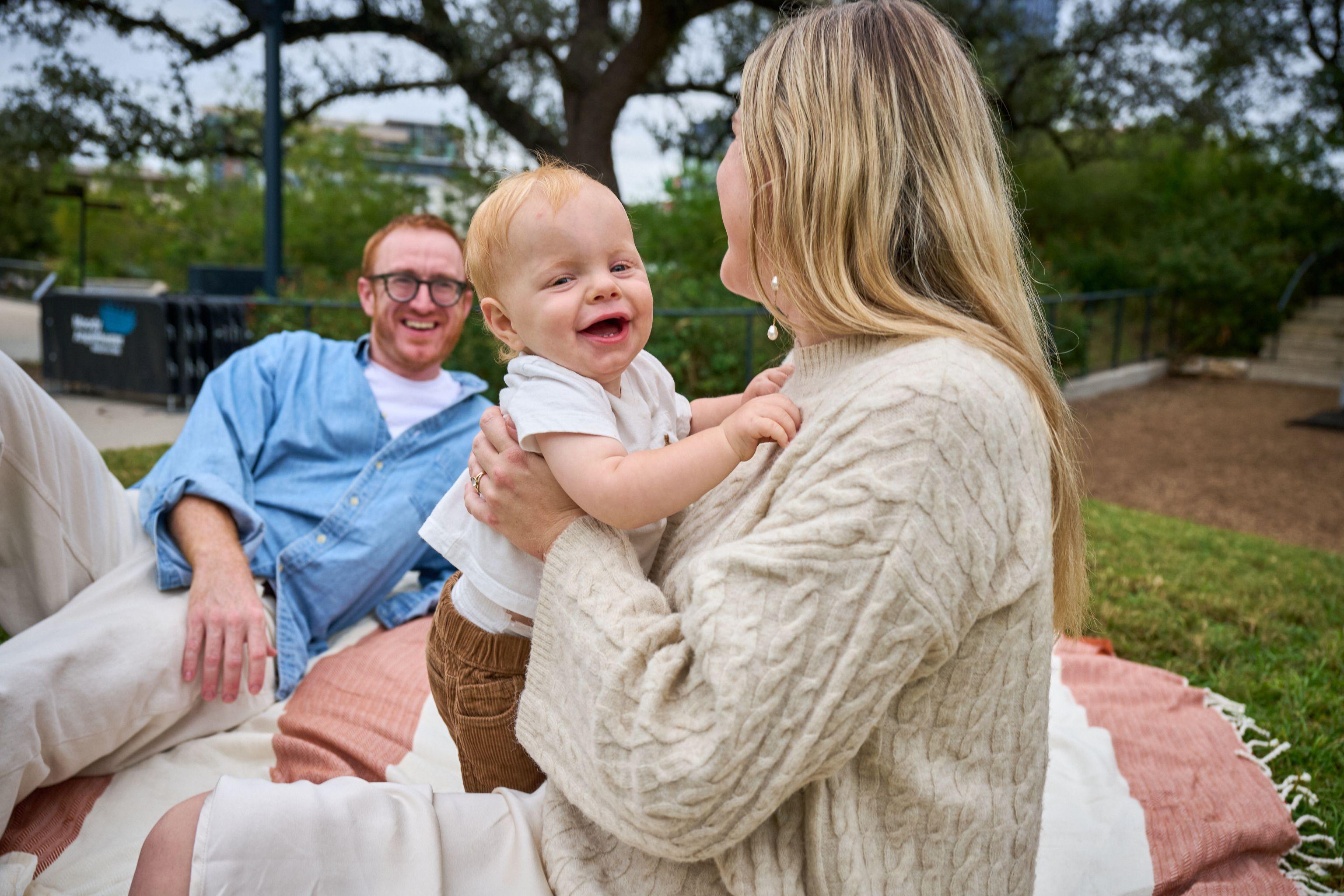 Mother holding her laughing baby while the father leans — Waterloo Park photography, Austin A mother holding her laughing baby while the father leans in behind.