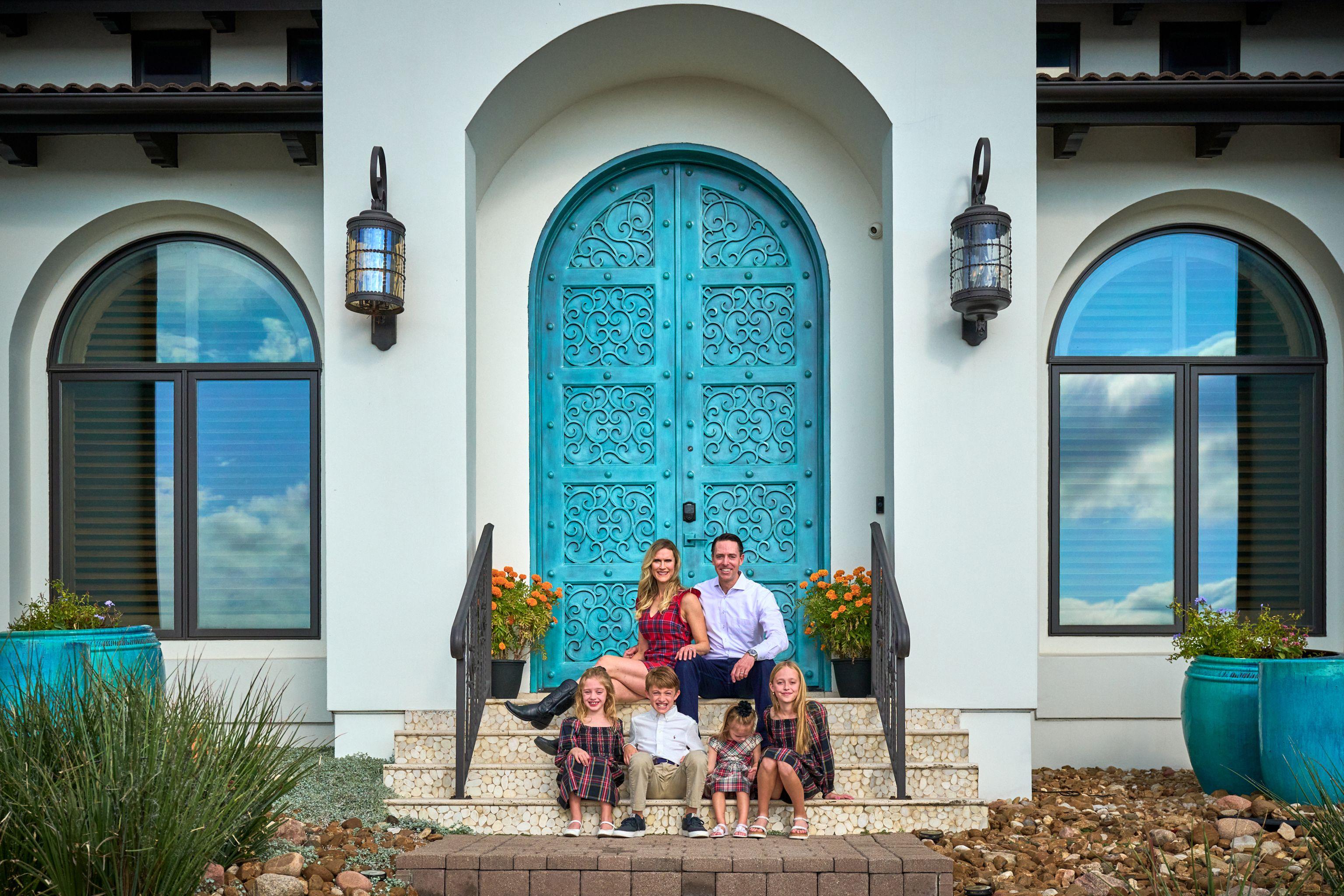 Family seated on the steps of a white house with ornate turquoise doors — Family Portraits photography, Austin A family seated on the steps of a white house with ornate turquoise doors.