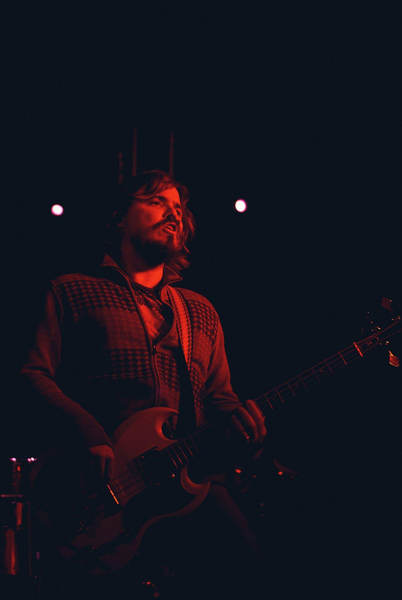 Guitarist lit in deep red on a dark stage — Live music photography, Austin A guitarist lit in deep red on a dark stage.
