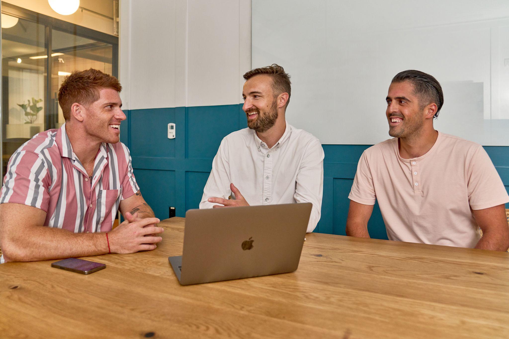 Man smiling at an open laptop during a meeting in front of a teal wall — Team offsite photography, Austin Man smiling at an open laptop during a meeting in front of a teal wall