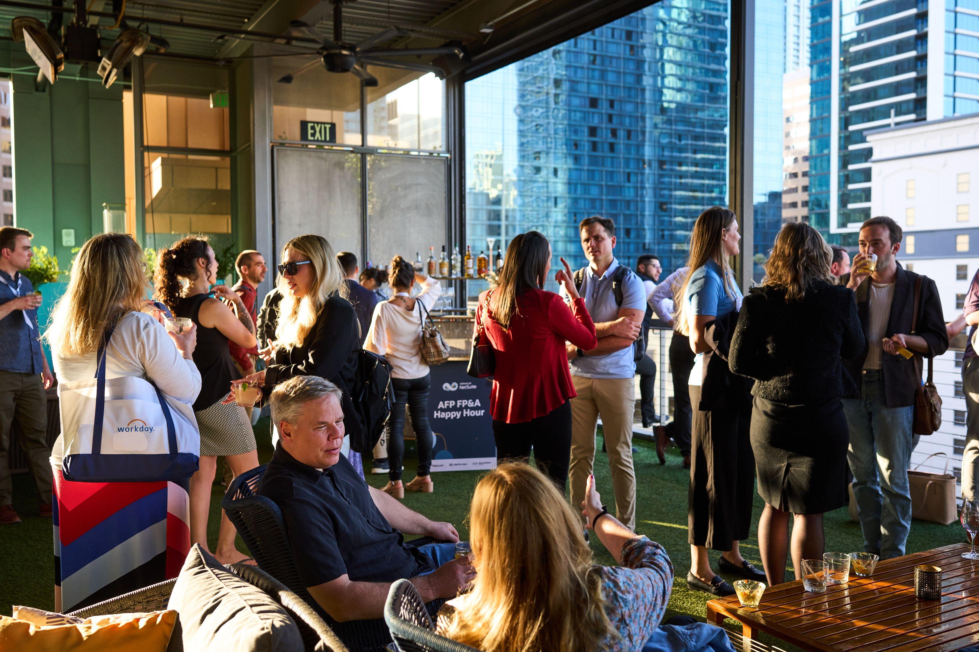 Colleagues talking and seated in low chairs on a rooftop terrace — Business Parties photography, Austin Colleagues talking and seated in low chairs on a rooftop terrace with downtown Austin towers behind.
