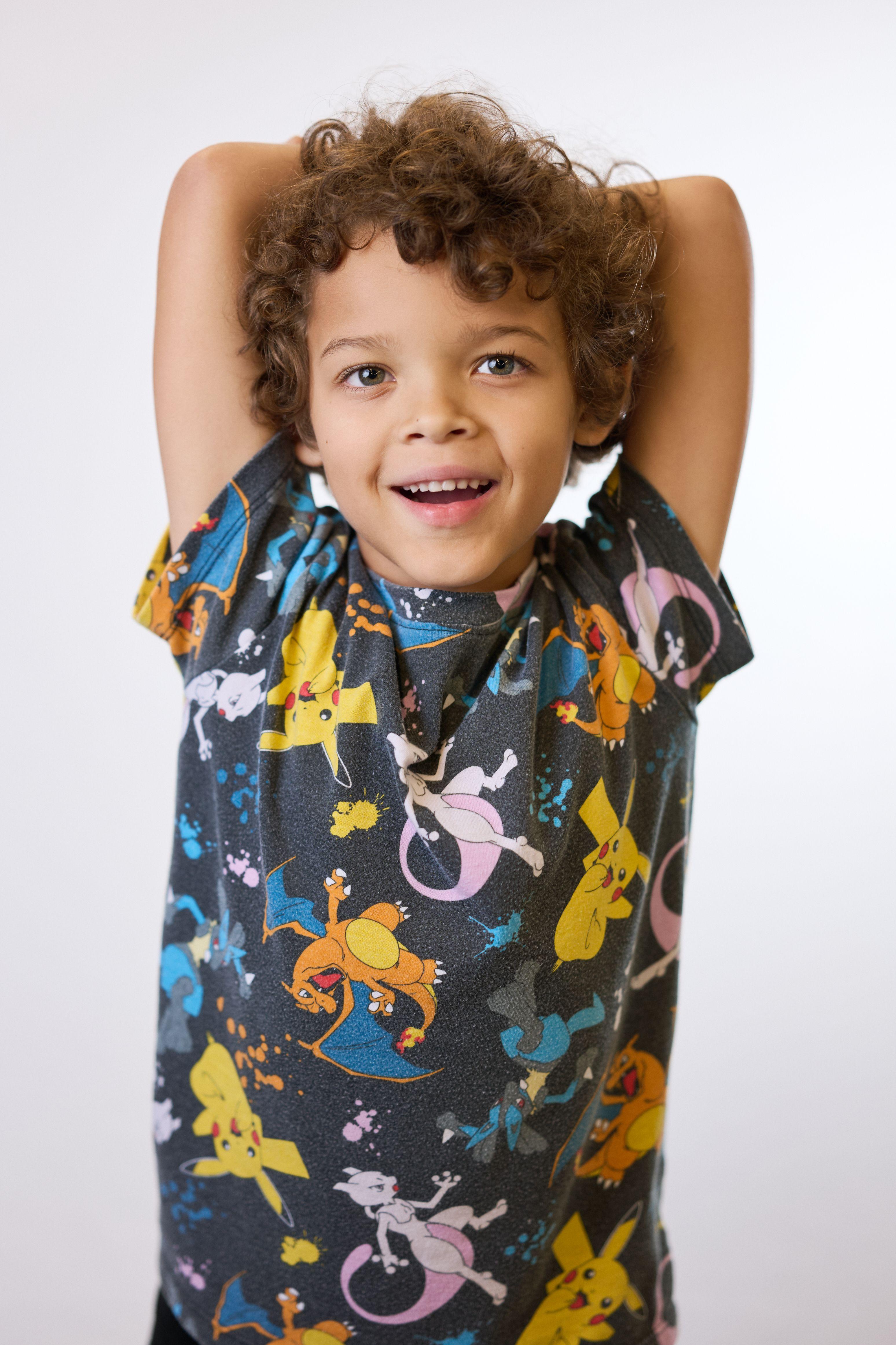 Young boy in a bright printed shirt with both arms raised above his head on white seamless — Commercial photo studio, Austin Young boy in a bright printed shirt with both arms raised above his head on white seamless