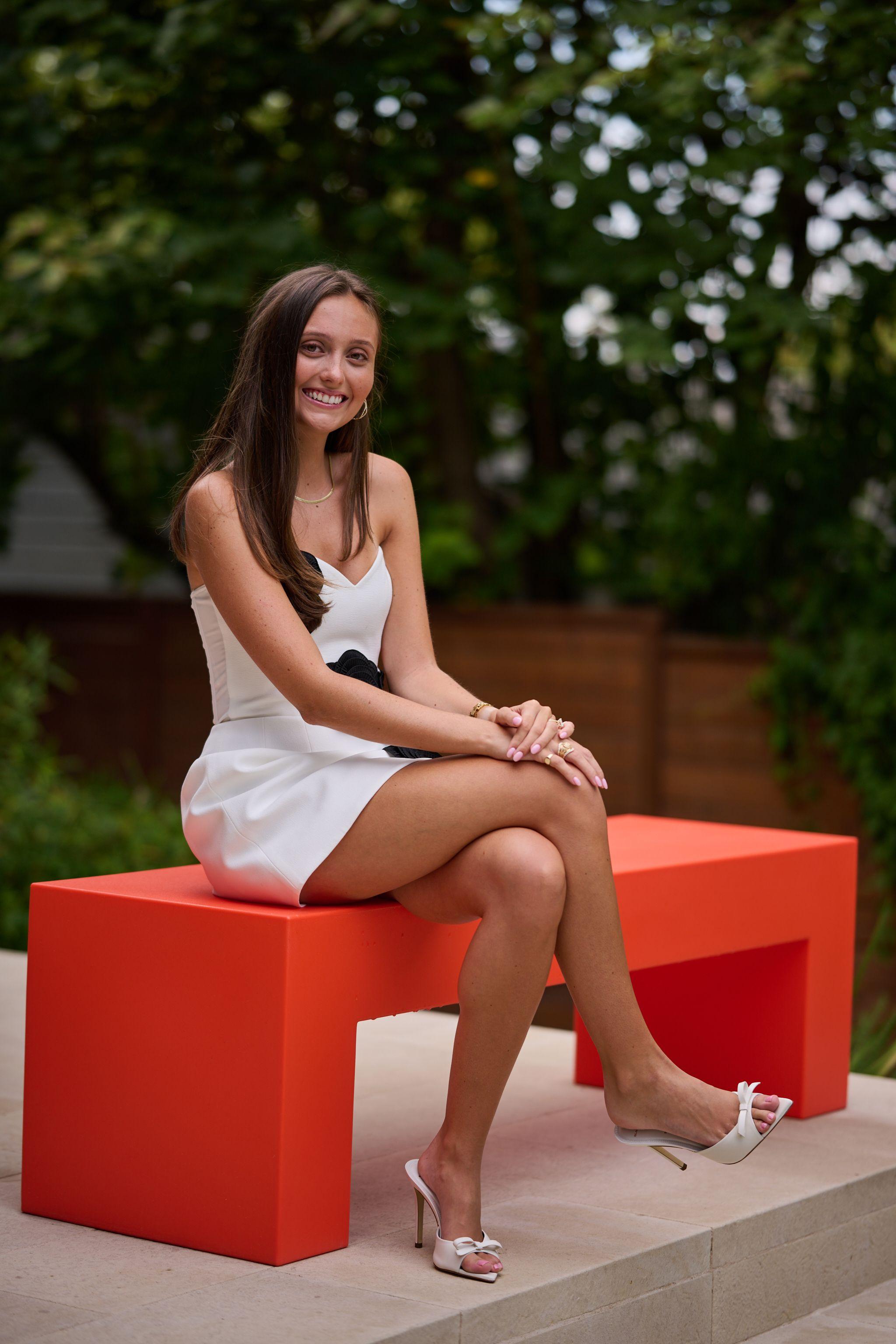 Young woman in a white dress seated on a bright orange bench in a garden — Formal Celebrations photography, Austin A young woman in a white dress seated on a bright orange bench in a garden.