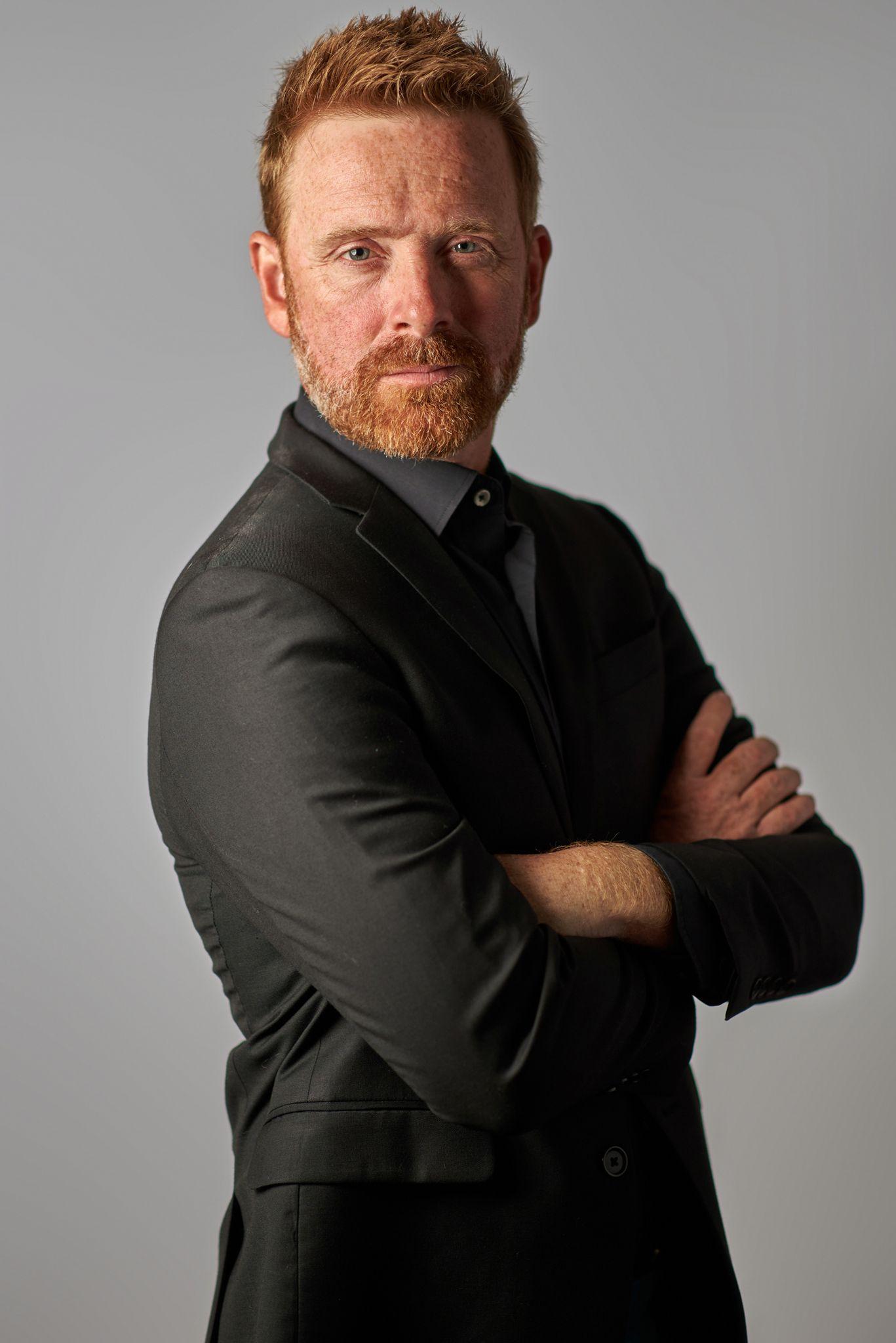 Bearded man in a black suit standing with arms crossed against a gray studio backdrop — Headshot photography, Austin Headshots