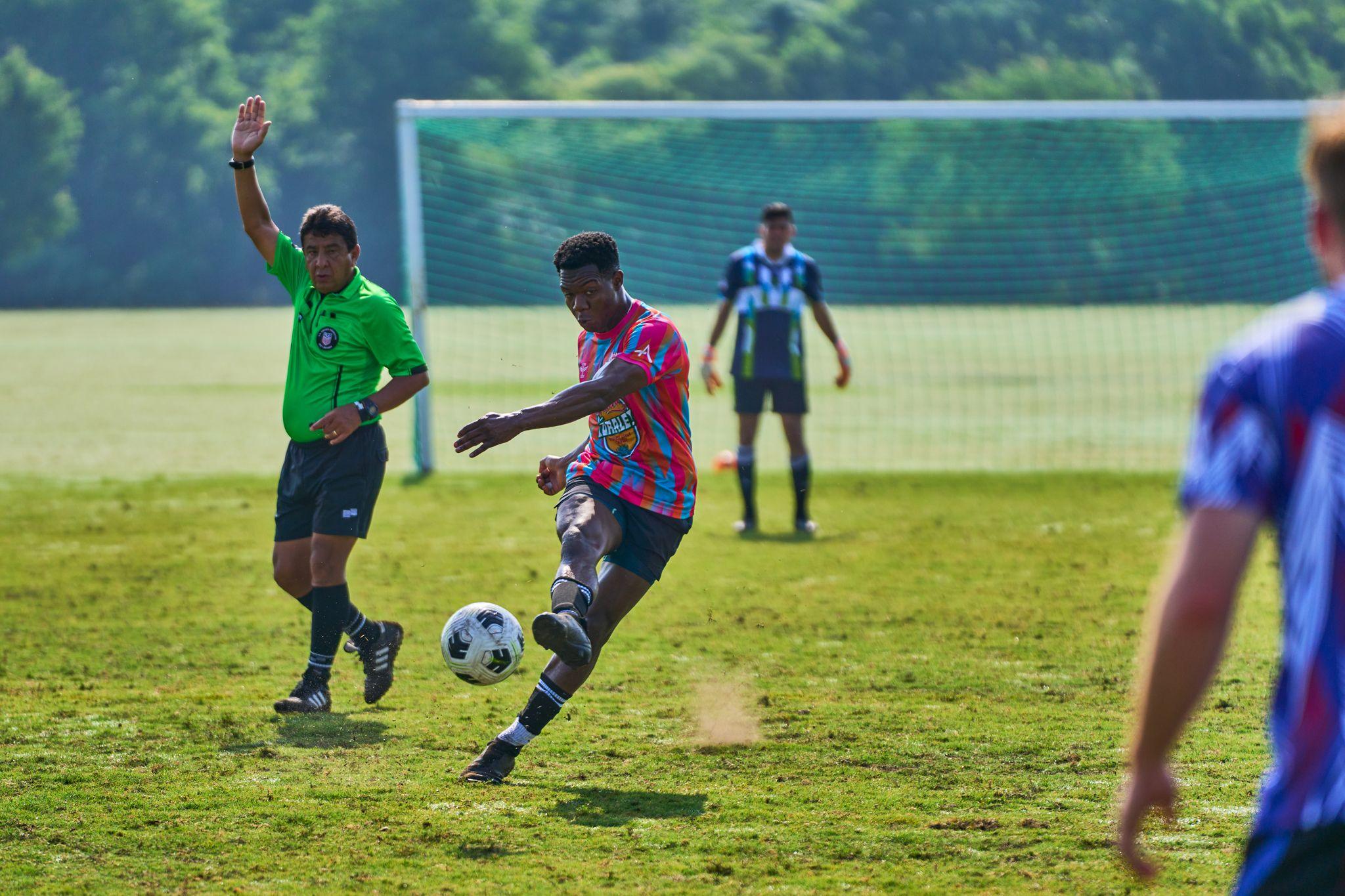 Footballer in a pink patterned kit striking the ball in front of an open goal — Sports photography, Austin Footballer in a pink patterned kit striking the ball in front of an open goal