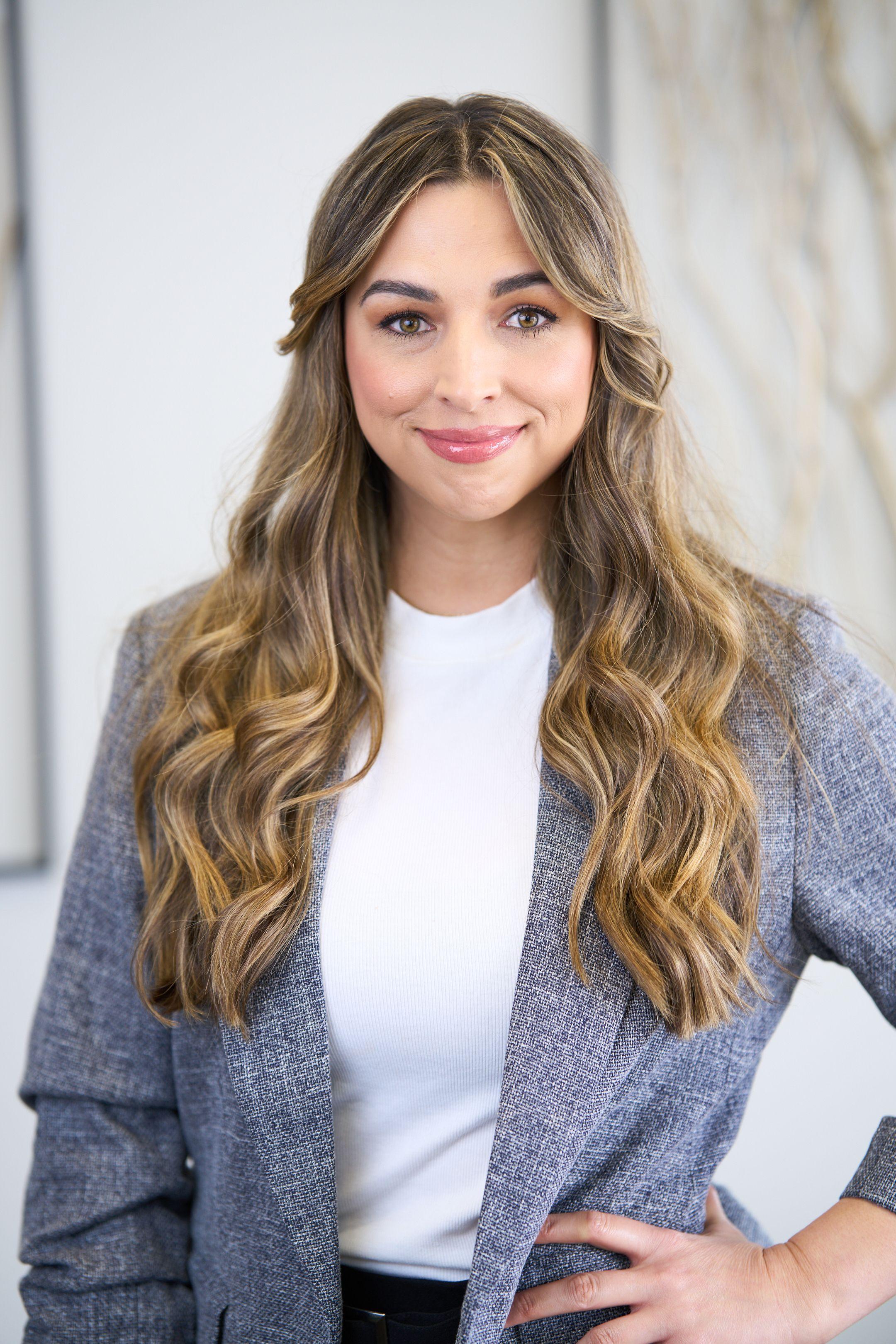 Clinician in a gray cardigan over a white top, smiling, photographed against a marble wall — Medical team photography, Austin Clinician in a gray cardigan over a white top, smiling, photographed against a marble wall