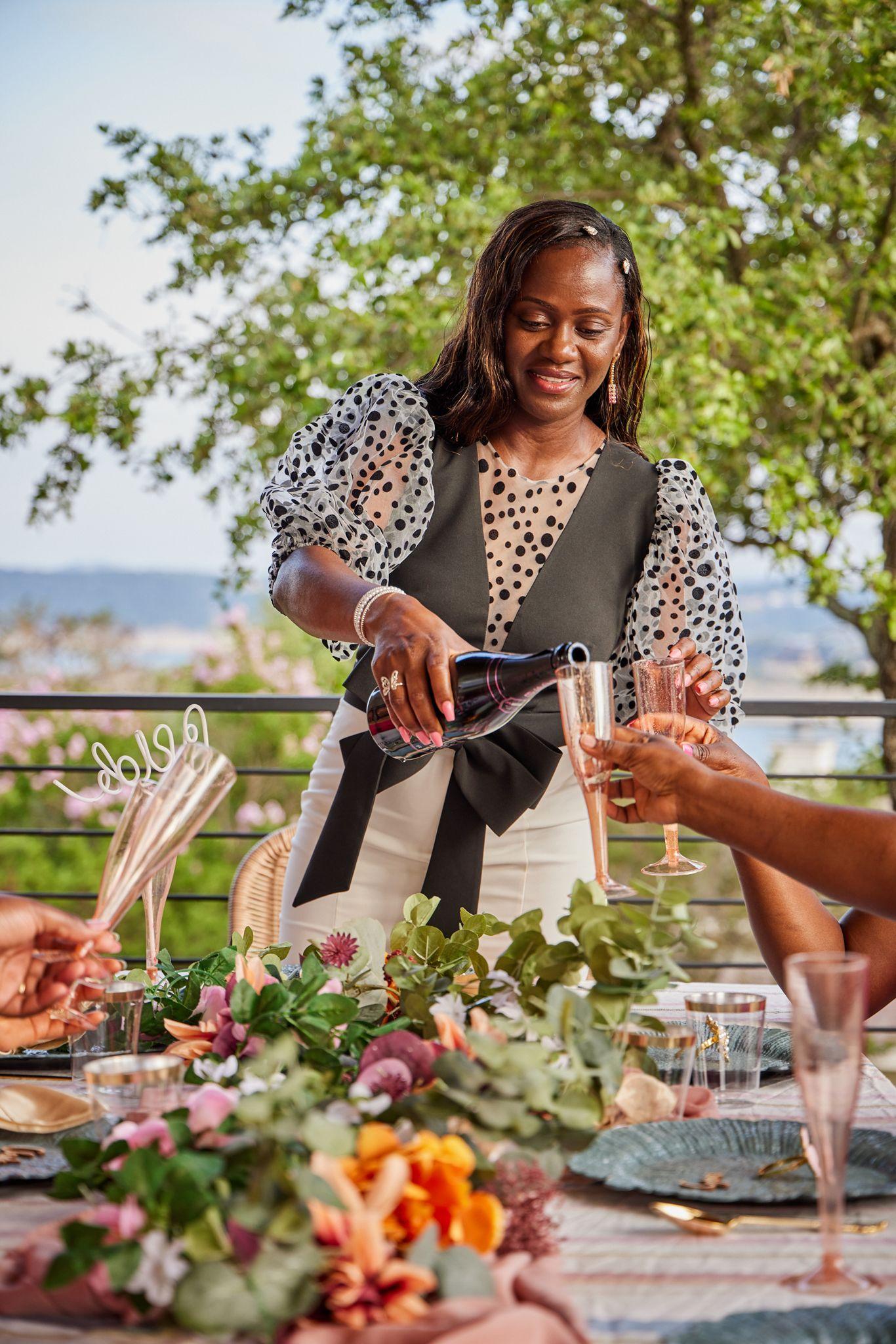 Host pouring champagne at a flower-covered outdoor table above the hills — Formal Celebrations photography, Austin A host pouring champagne at a flower-covered outdoor table above the hills.