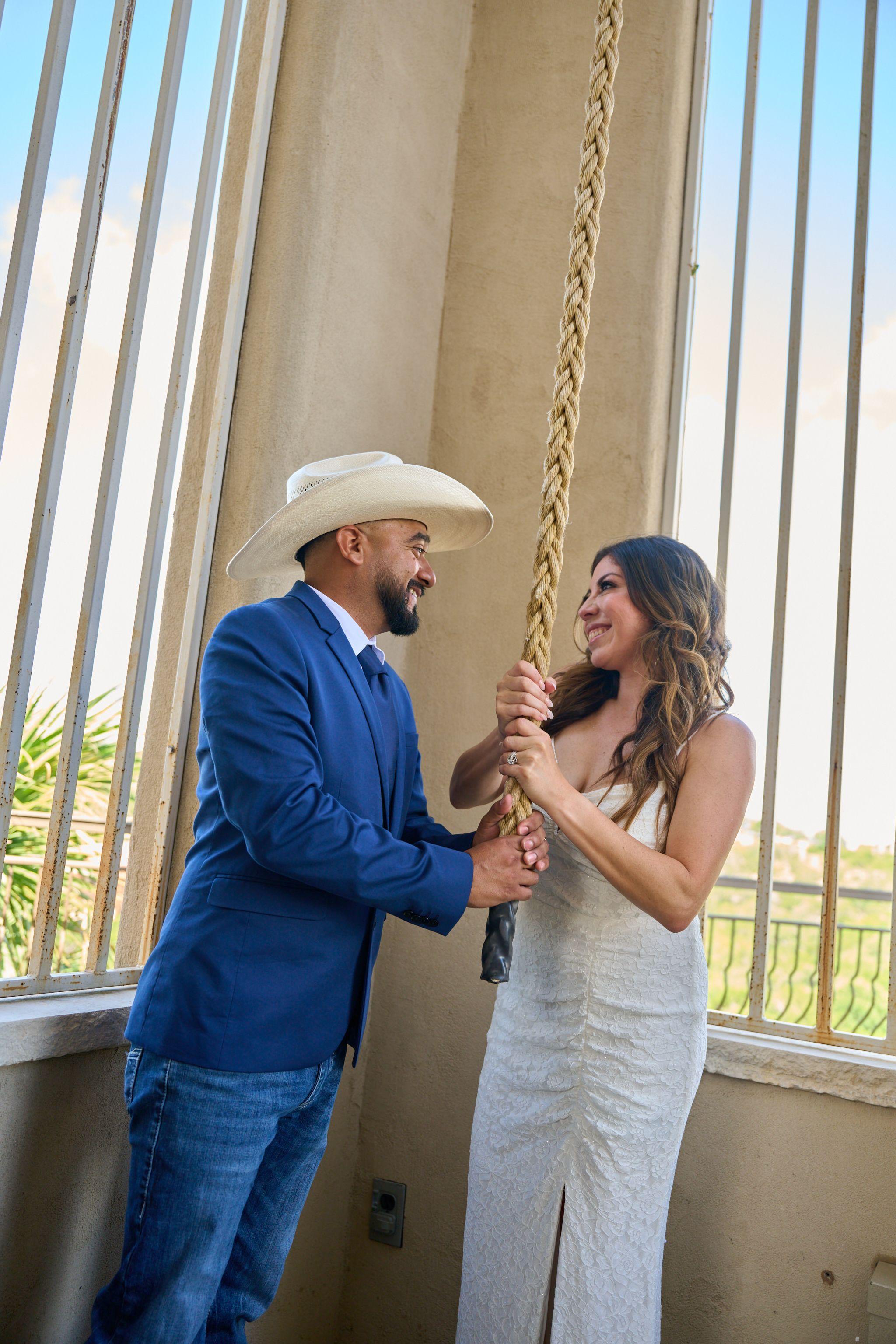 Groom in a cowboy hat and blue suit taking the chapel bell rope with his bride — Chapel Dulcinea photography, Austin A groom in a cowboy hat and blue suit taking the chapel bell rope with his bride.