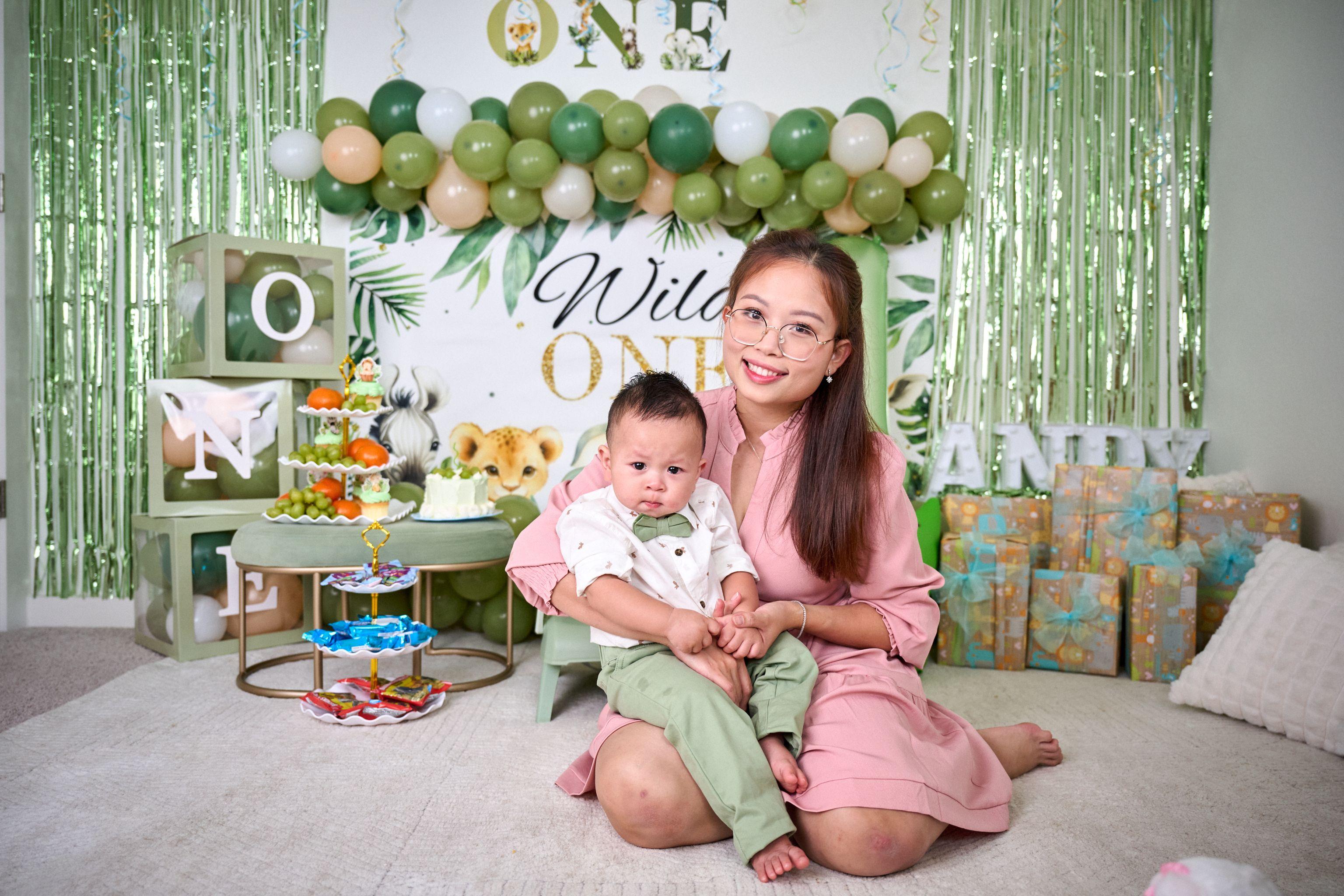 Mother seated with her baby in front of a 'Wild ONE' balloon arch and jungle backdrop — Family Parties photography, Austin A mother seated with her baby in front of a 'Wild ONE' balloon arch and jungle backdrop.