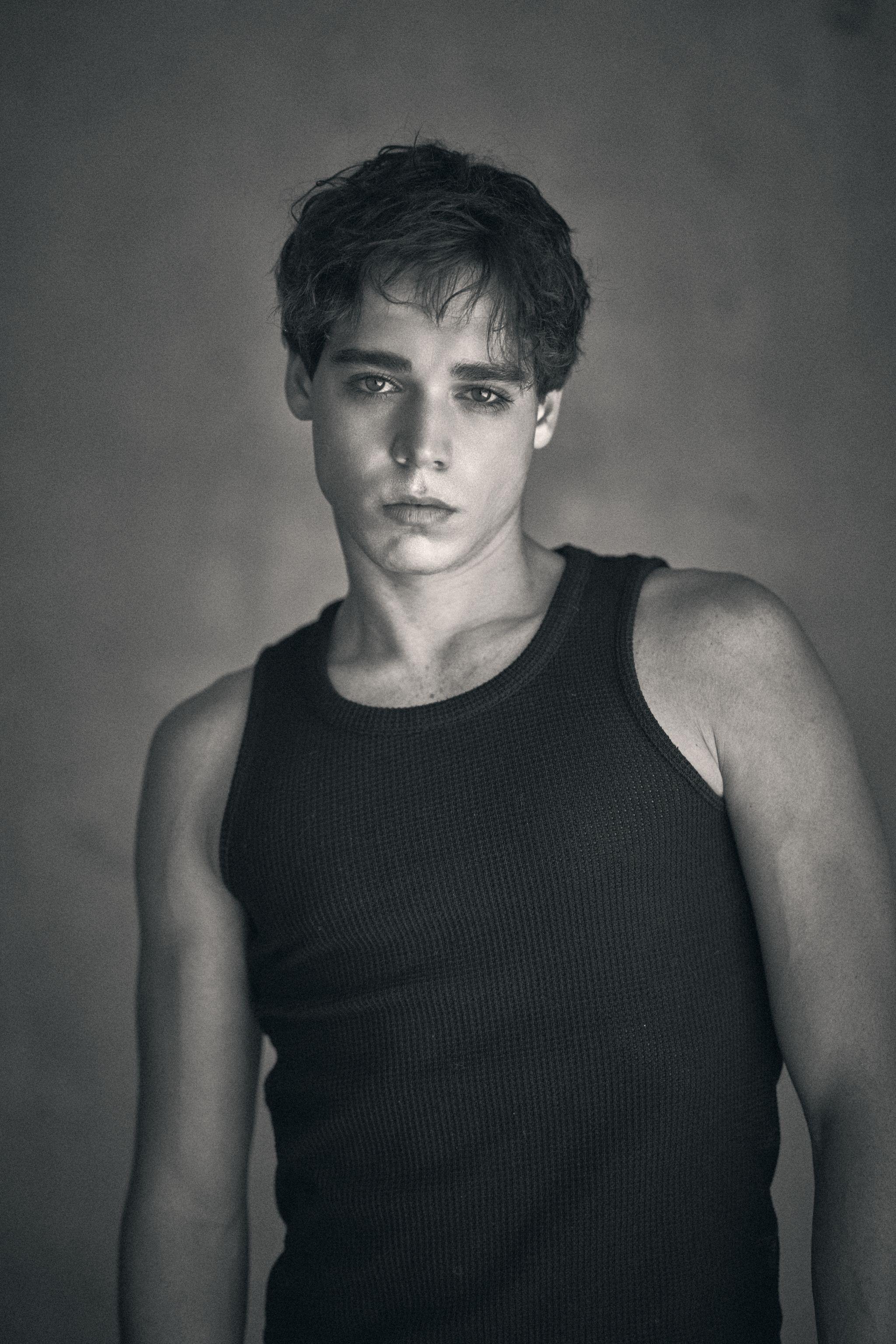 Black and white portrait of a male model in a black tank top against a dark studio background — Fashion & editorial photography, Austin A black and white portrait of a male model in a black tank top against a dark studio background.