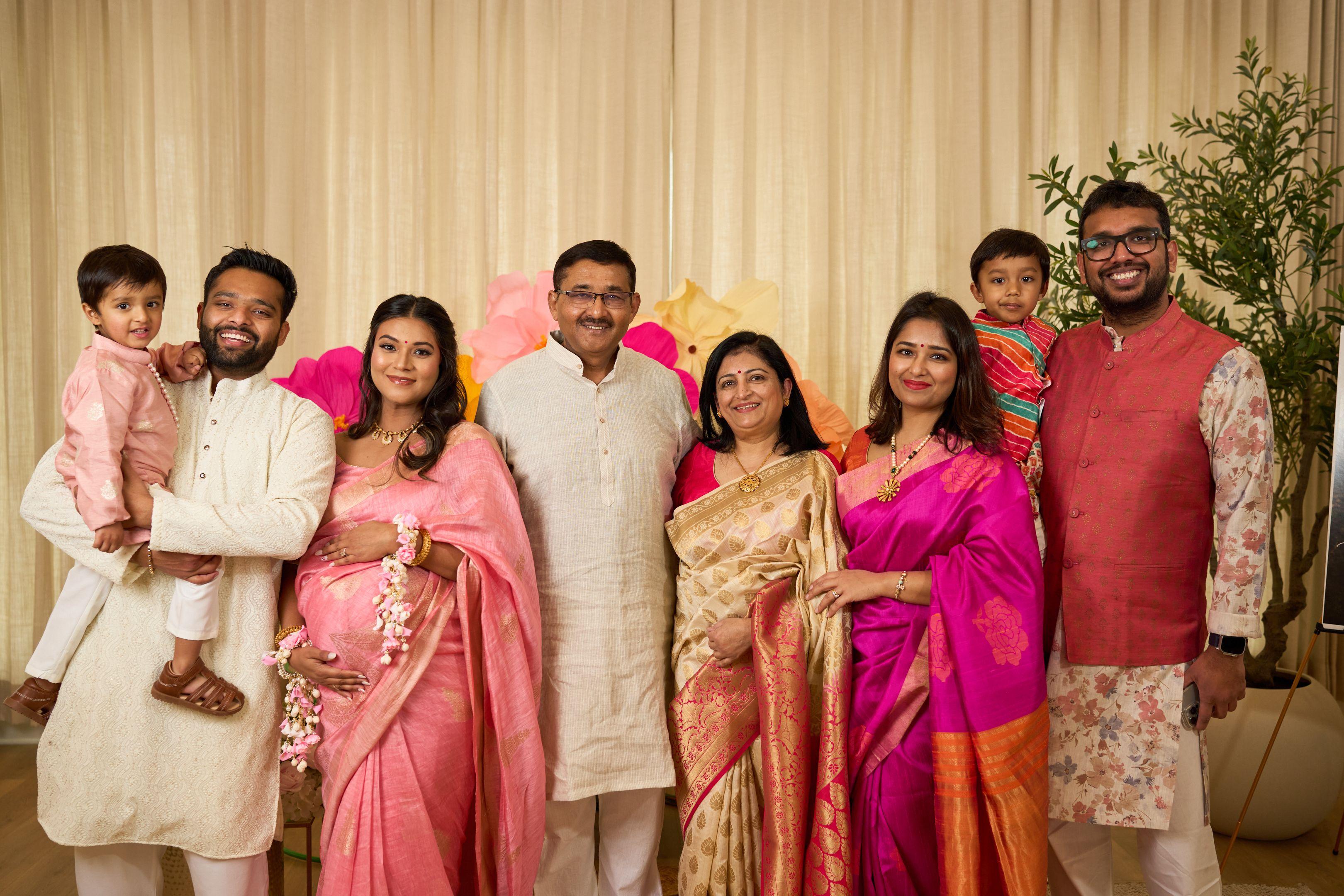 Family in sarees at a baby shower behind a floral backdrop — Maternity photography, Austin Family in sarees at a baby shower behind a floral backdrop