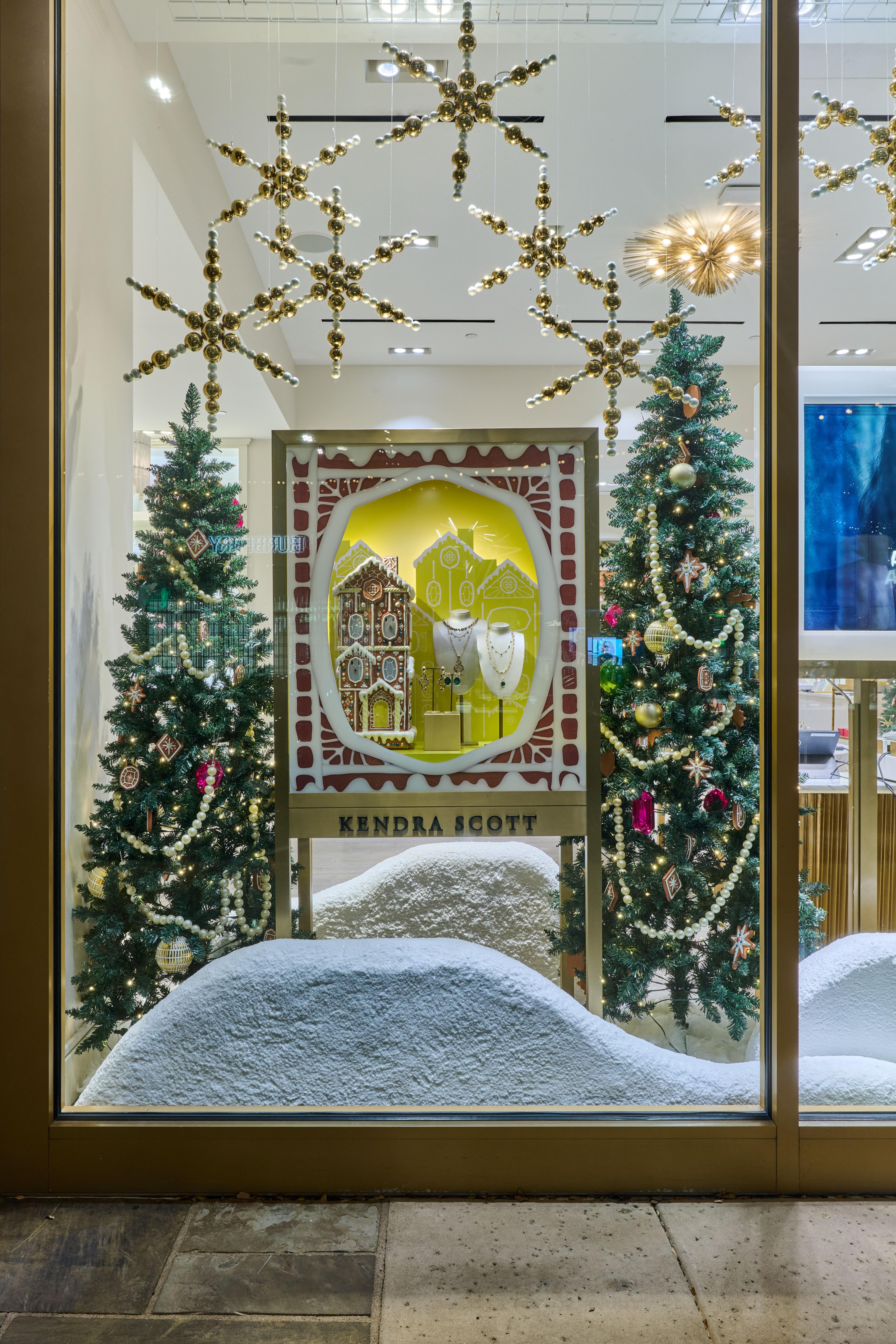 Holiday storefront window with flocked Christmas trees framing a gold gingerbread-house display — Brand Collaborations photography, Austin A holiday storefront window with flocked Christmas trees framing a gold gingerbread-house display at Kendra Scott.