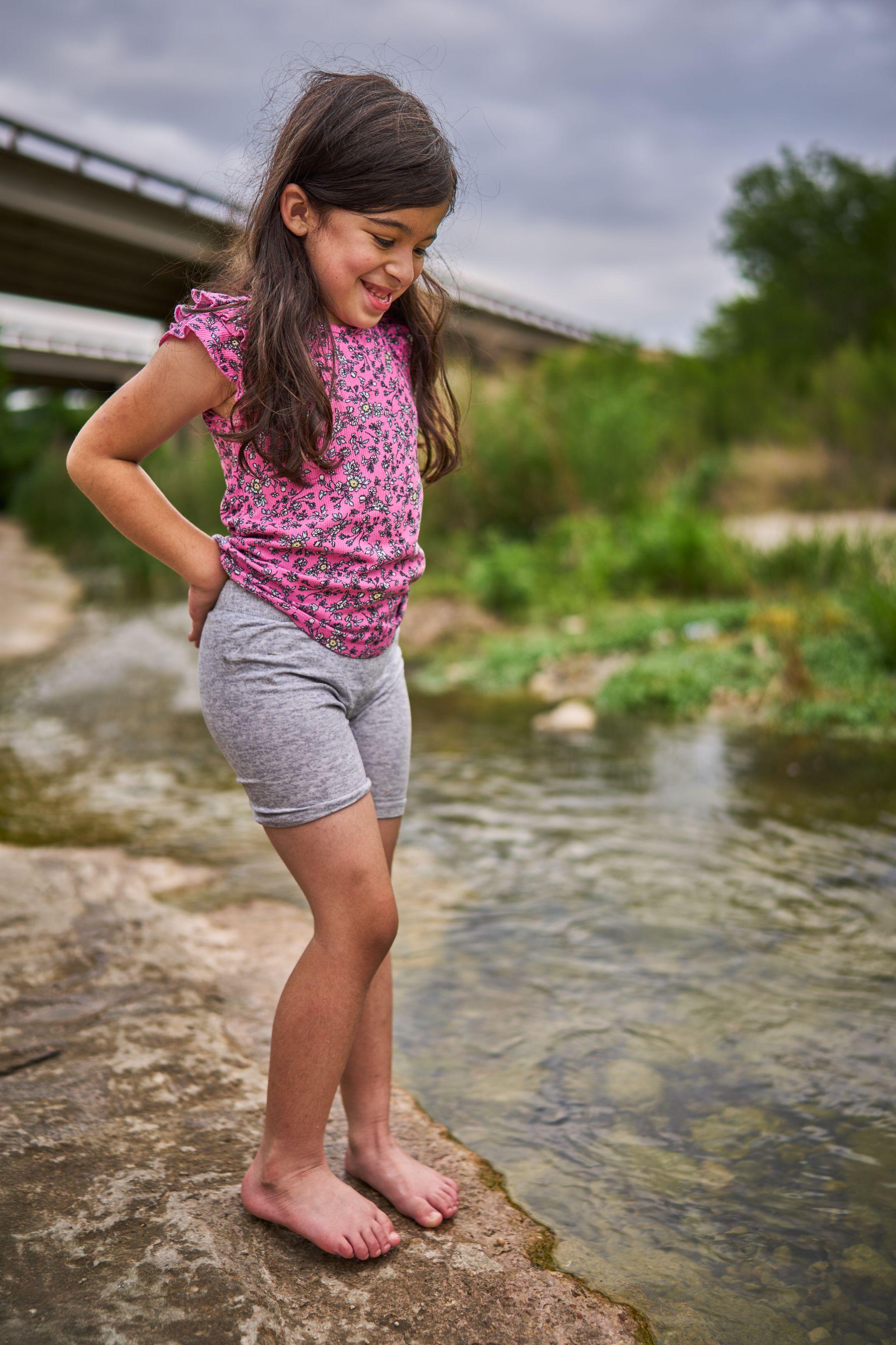 Girl in pink standing hands-on-hips on a rock beside a creek — Bull Creek District Park photography, Austin A girl in pink standing hands-on-hips on a rock beside a creek.