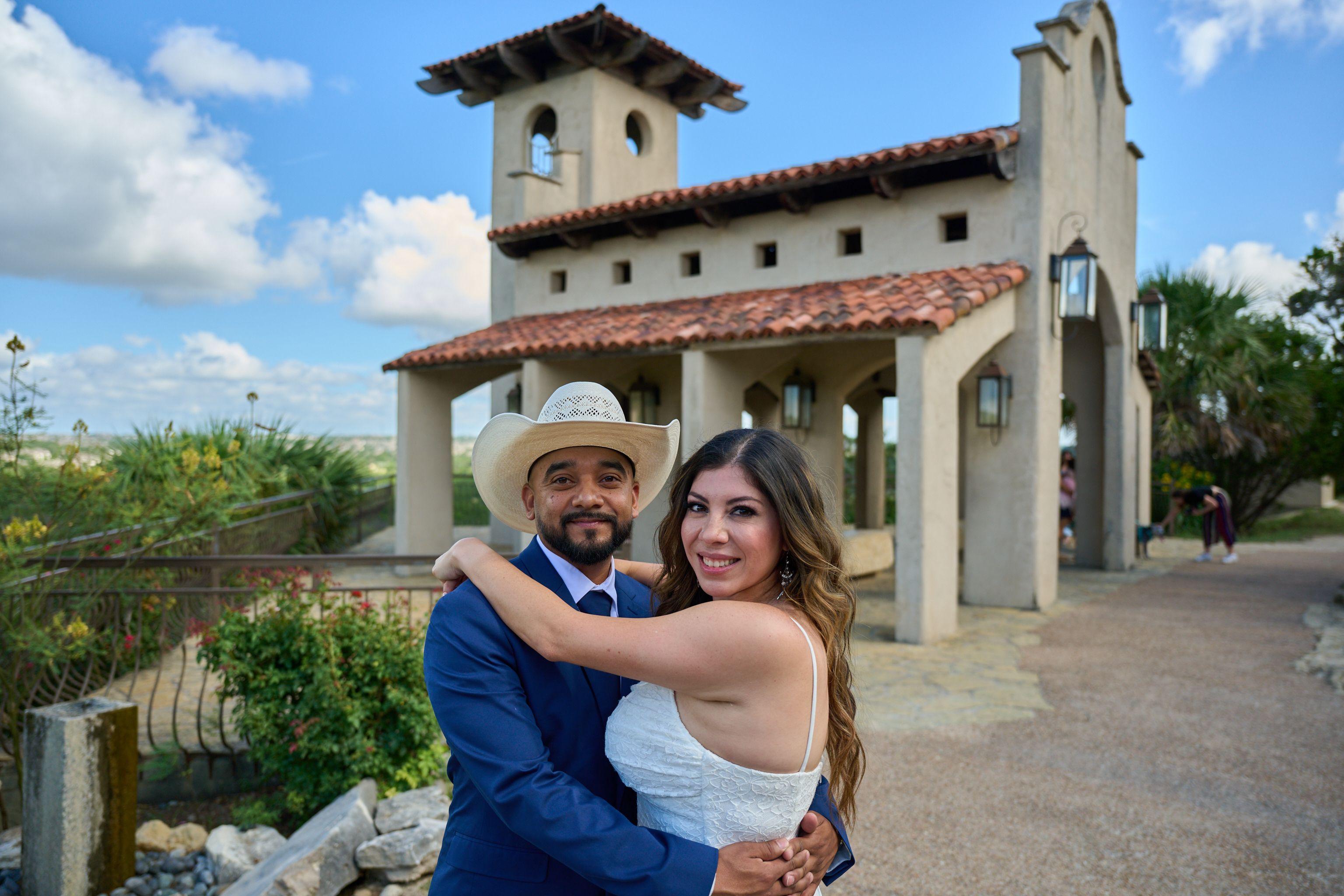 Couple embracing outside the Chapel Dulcinea bell tower, the groom in a straw cowboy hat — Chapel Dulcinea photography, Austin A couple embracing outside the Chapel Dulcinea bell tower, the groom in a straw cowboy hat.
