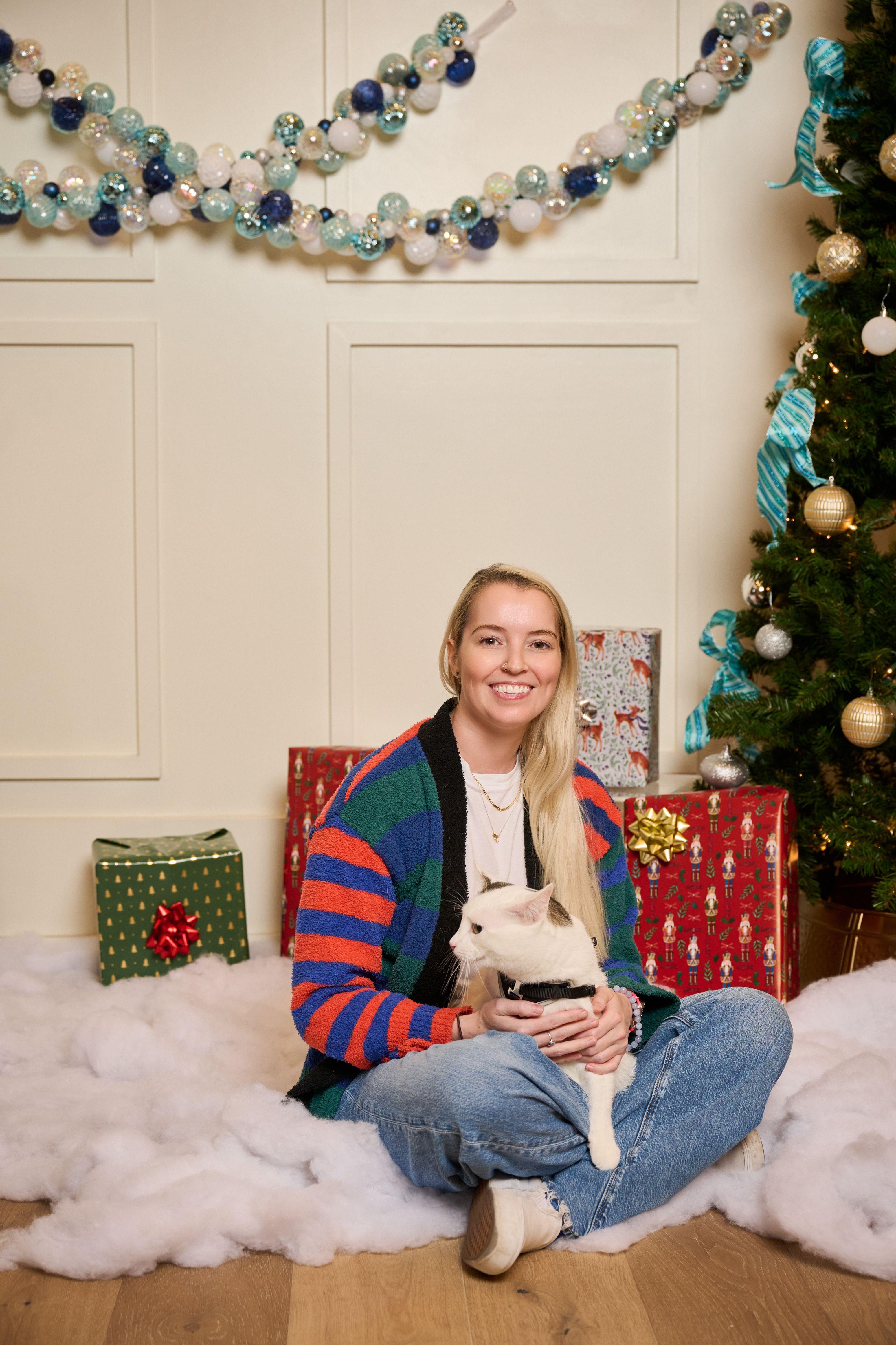 Woman sitting on artificial snow holding a small white dog, wrapped presents — Mobile photo studio, Austin A woman sitting on artificial snow holding a small white dog, wrapped presents and a Christmas tree beside her