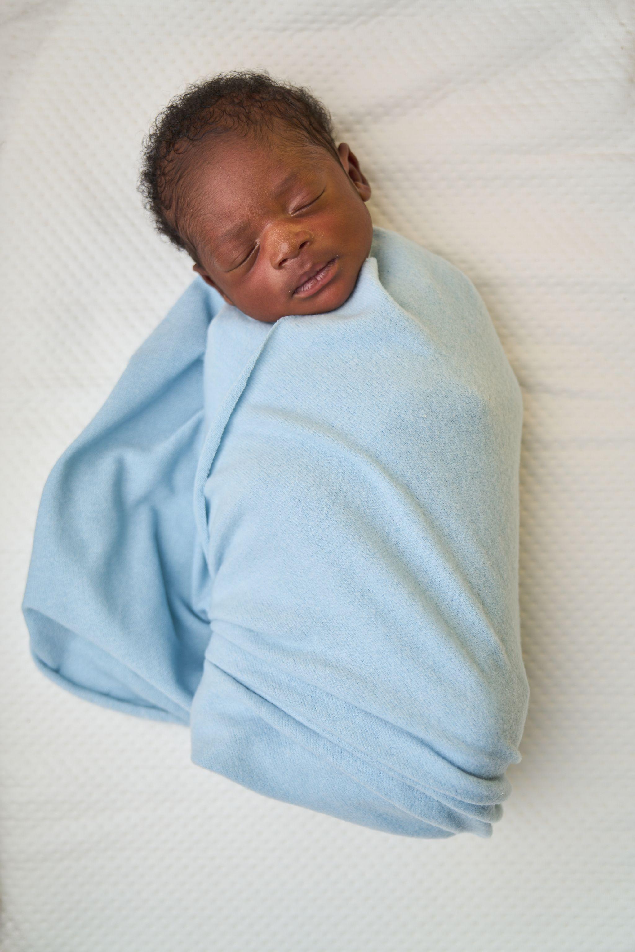 Newborn swaddled in a pale blue wrap, asleep on white — Newborn photography, Austin A newborn swaddled in a pale blue wrap, asleep on white.