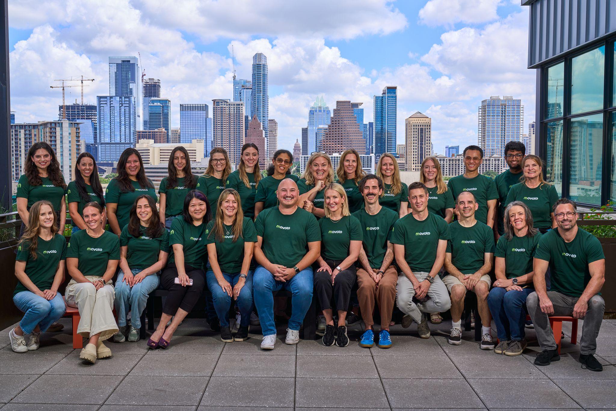 Company team in green branded shirts posed in rows outdoors with the Austin skyline behind them — Team photography, Austin Company team in green branded shirts posed in rows outdoors with the Austin skyline behind them