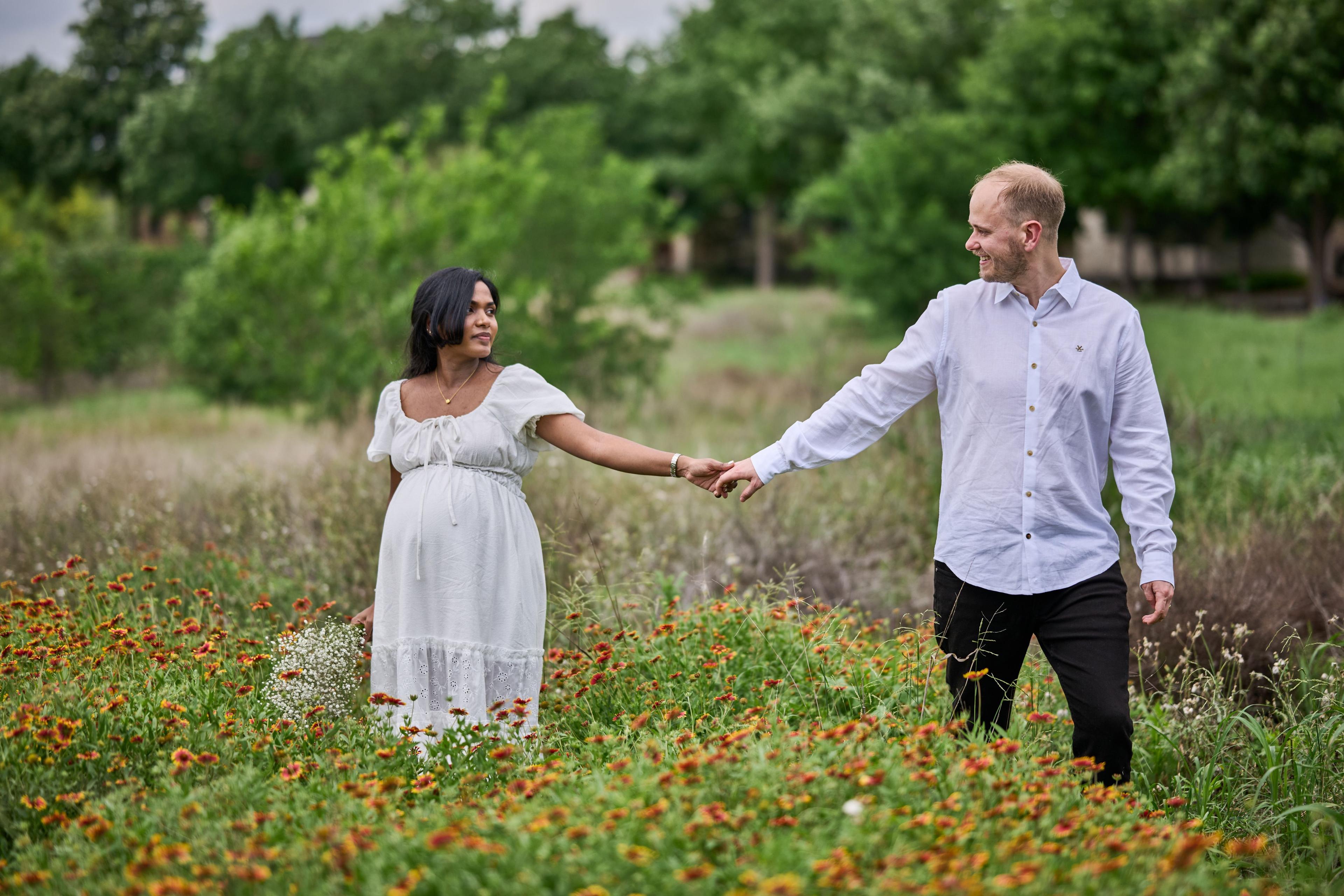 Expectant couple reaching for each other's hands in a field of orange wildflowers — Mueller Lake Park & Butterfly Garden photography, Austin An expectant couple reaching for each other's hands in a field of orange wildflowers.