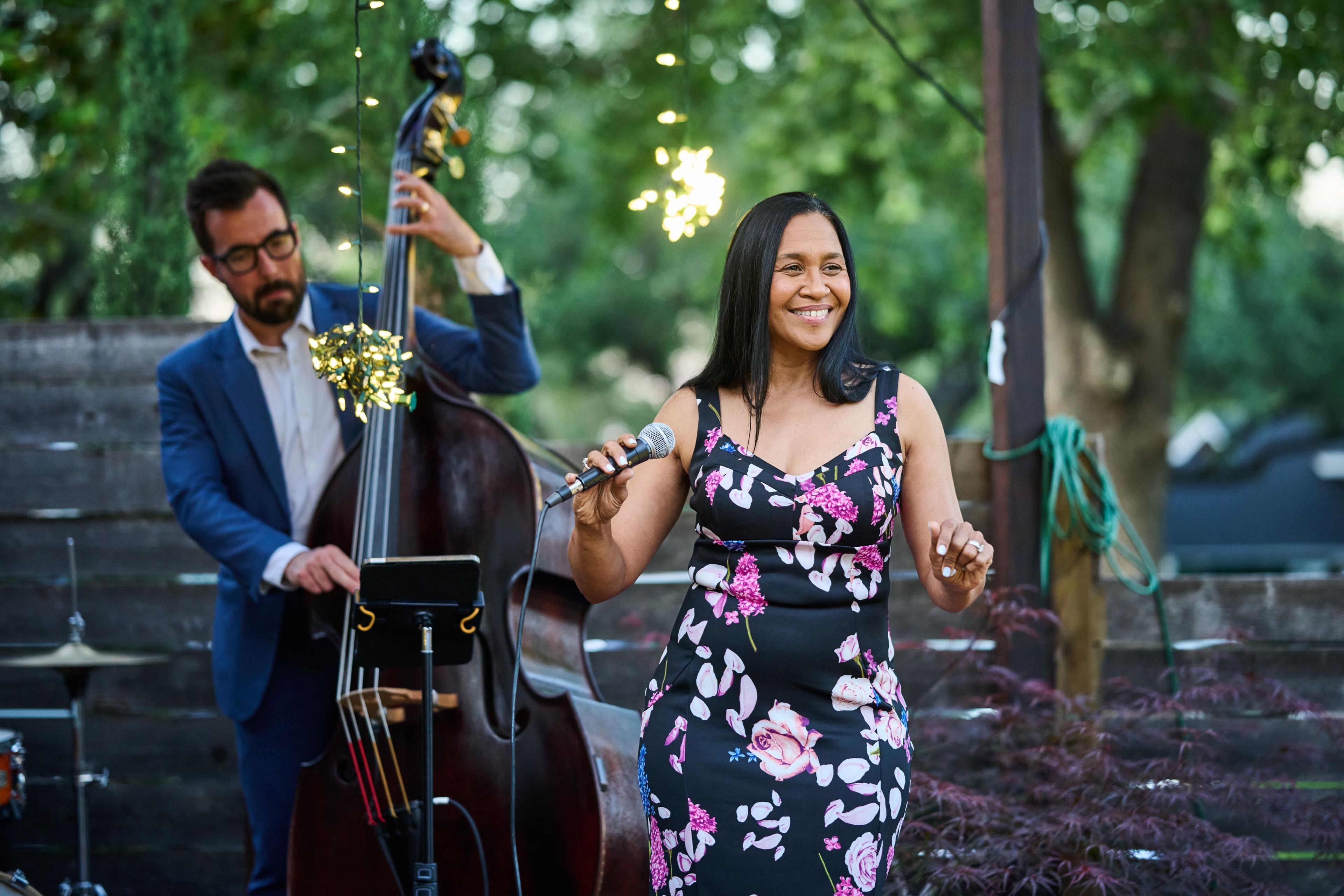 Singer in a floral dress performing beside a double bass under string lights — Formal Celebrations photography, Austin A singer in a floral dress performing beside a double bass under string lights.
