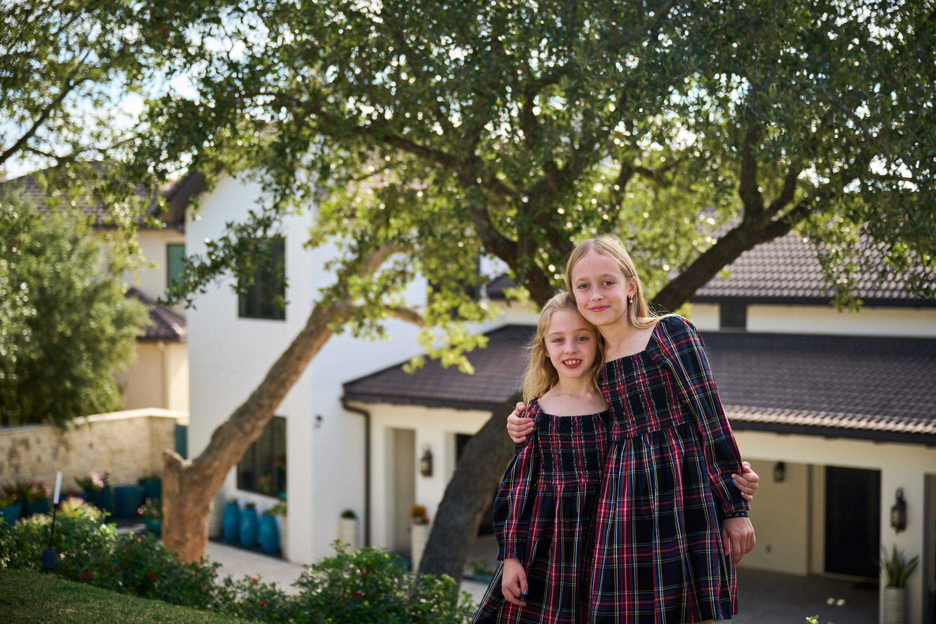 Two sisters in tartan dresses standing under an oak in front of a white house — Family Portraits photography, Austin Two sisters in tartan dresses standing under an oak in front of a white house.