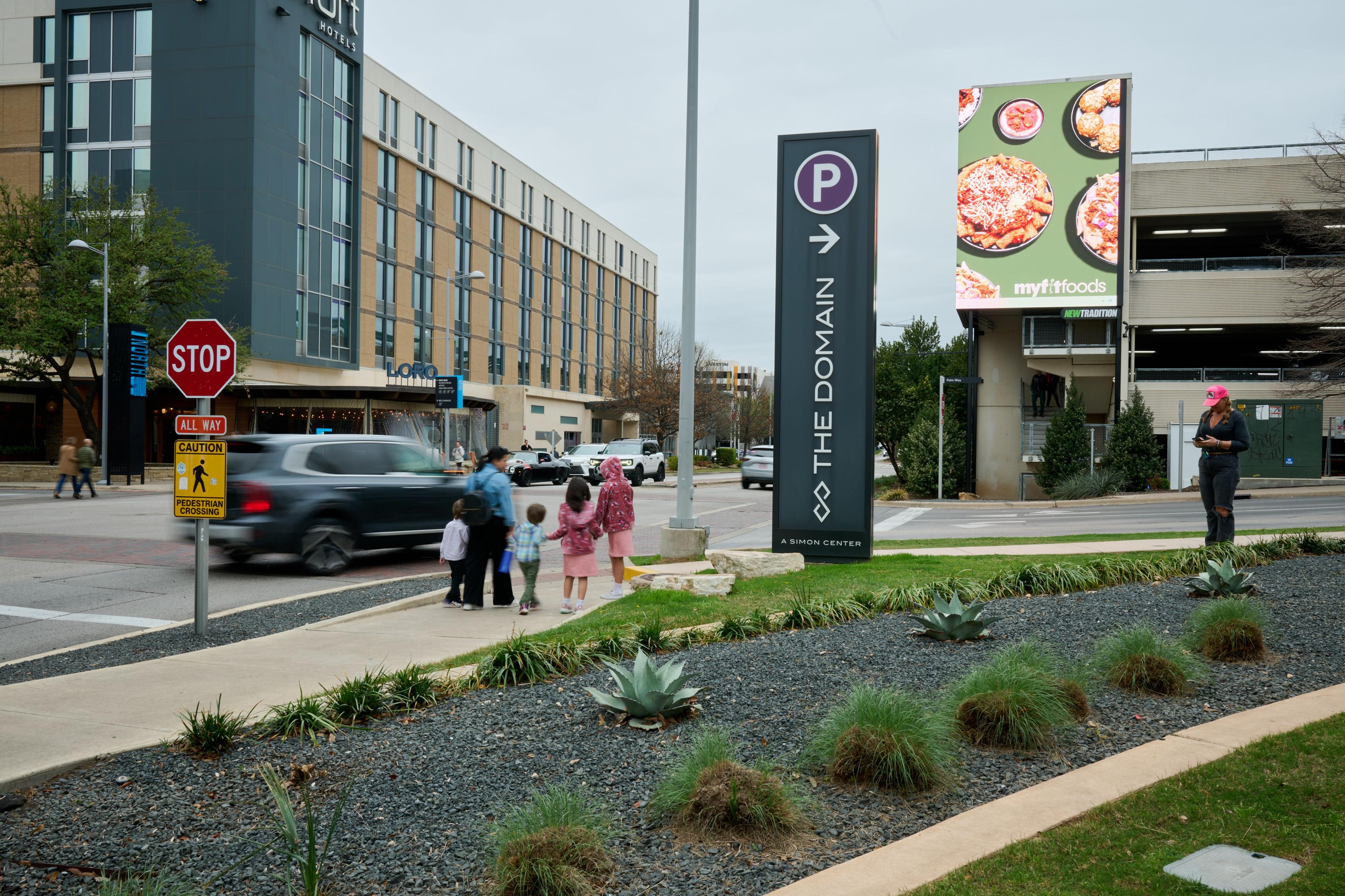 Family walking past The Domain's wayfinding sign, planting and parking markers along the street — The Domain photography, Austin A family walking past The Domain's wayfinding sign, planting and parking markers along the street