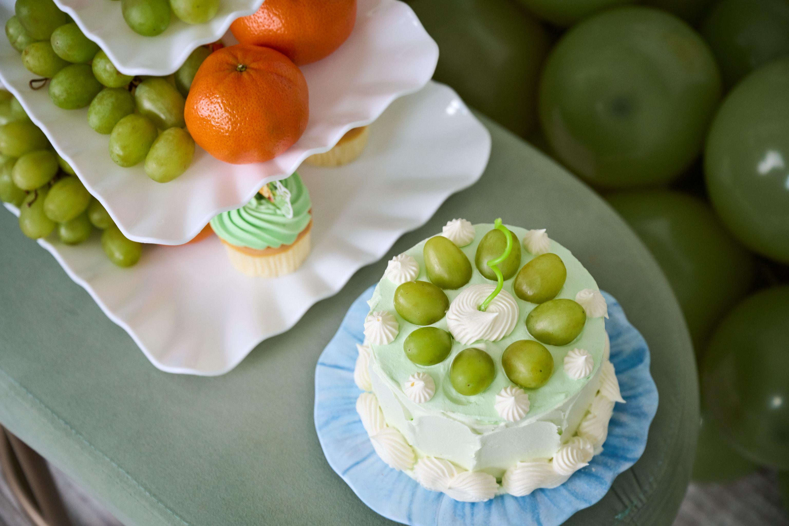 Green frosted cake decorated with grapes on a white plate, photographed beside cupcakes — Family Parties photography, Austin A green frosted cake decorated with grapes on a white plate, photographed beside cupcakes and clementines