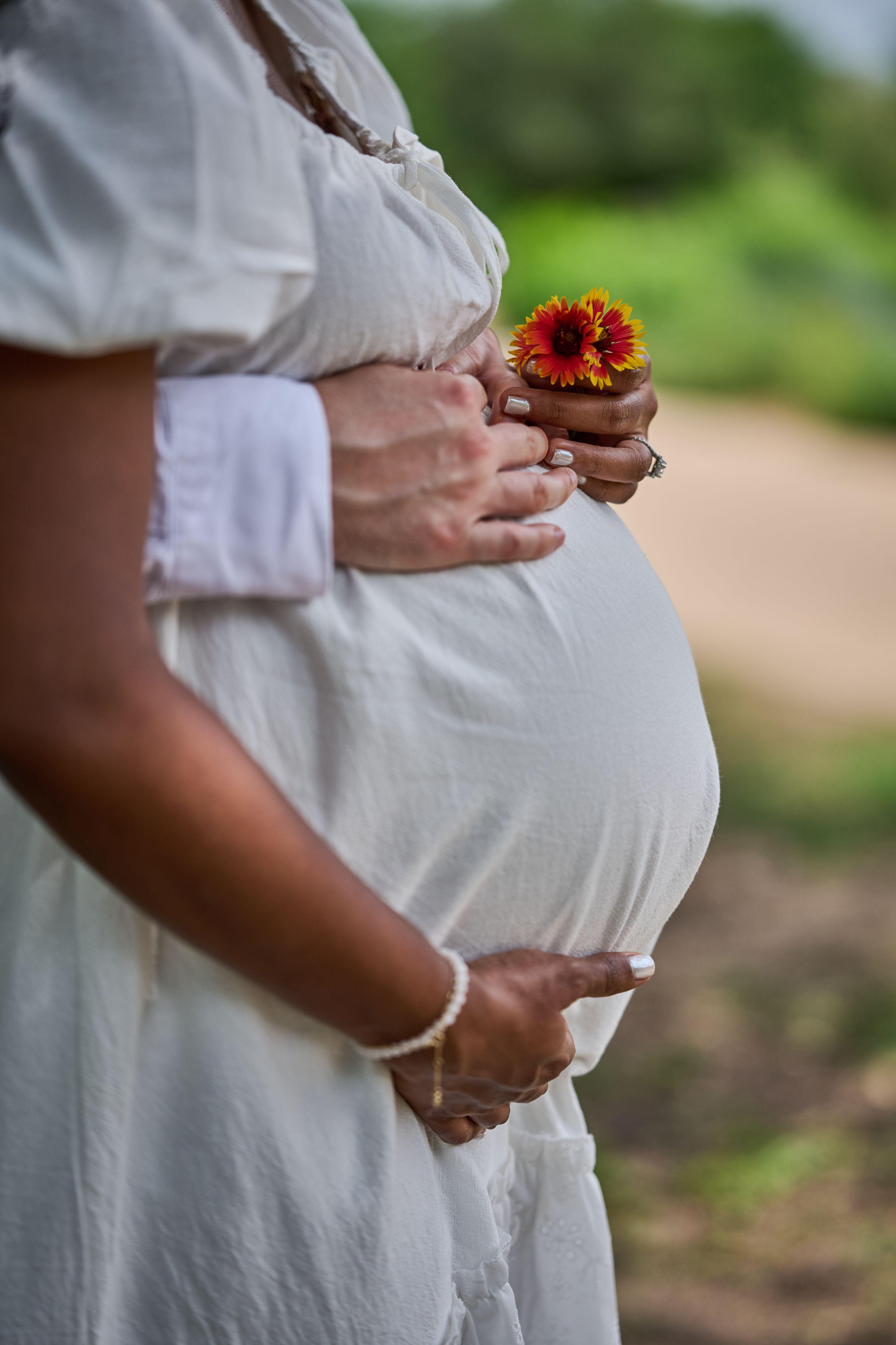 Close frame of an expectant mother's hands on her bump holding a single orange wildflower — Mueller Lake Park & Butterfly Garden photography, Austin A close frame of an expectant mother's hands on her bump holding a single orange wildflower
