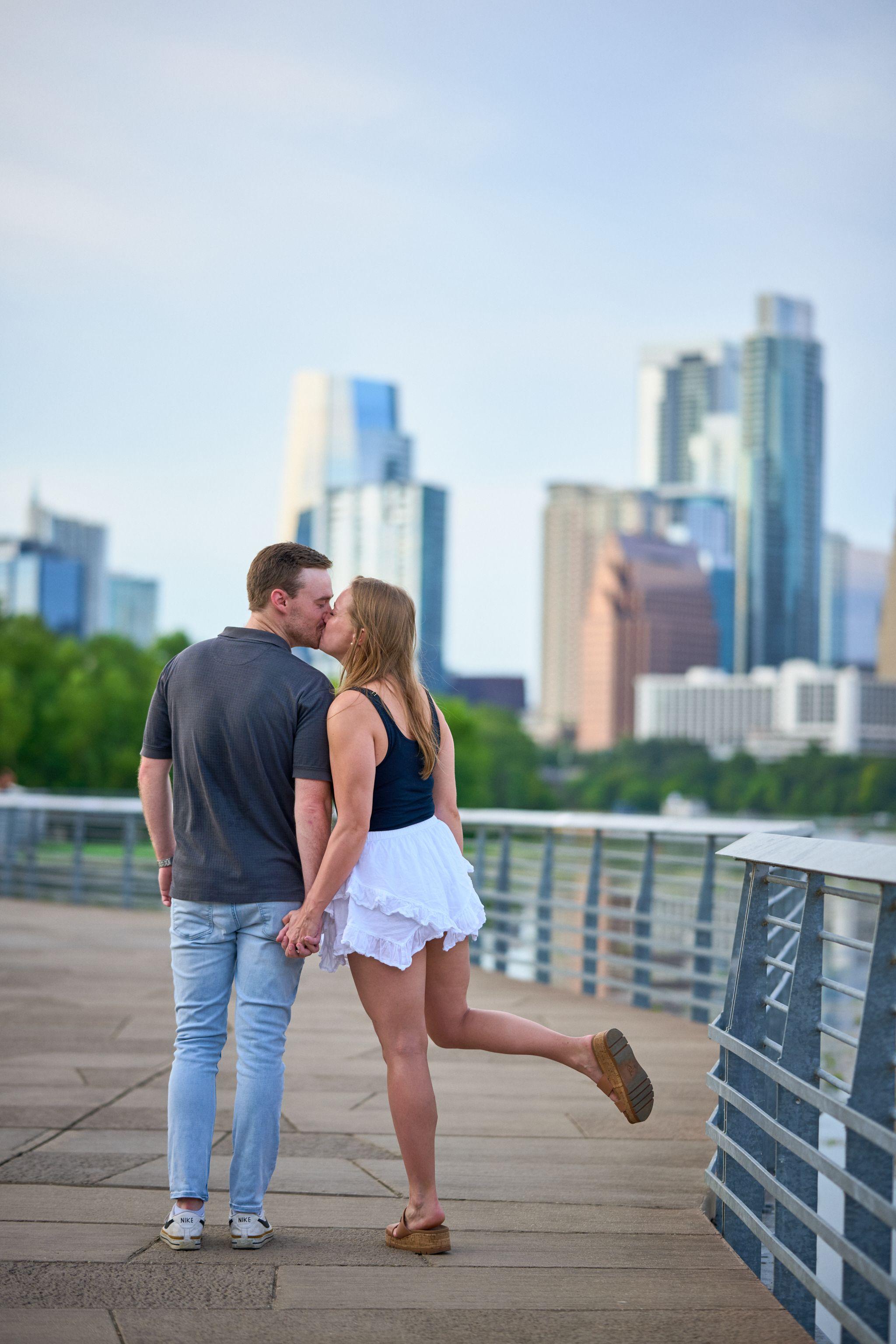 Couple kissing mid-stride on the Lady Bird Lake boardwalk — Austin Boardwalk photography, Austin A couple kissing mid-stride on the Lady Bird Lake boardwalk, the downtown Austin skyline filling the frame behind them