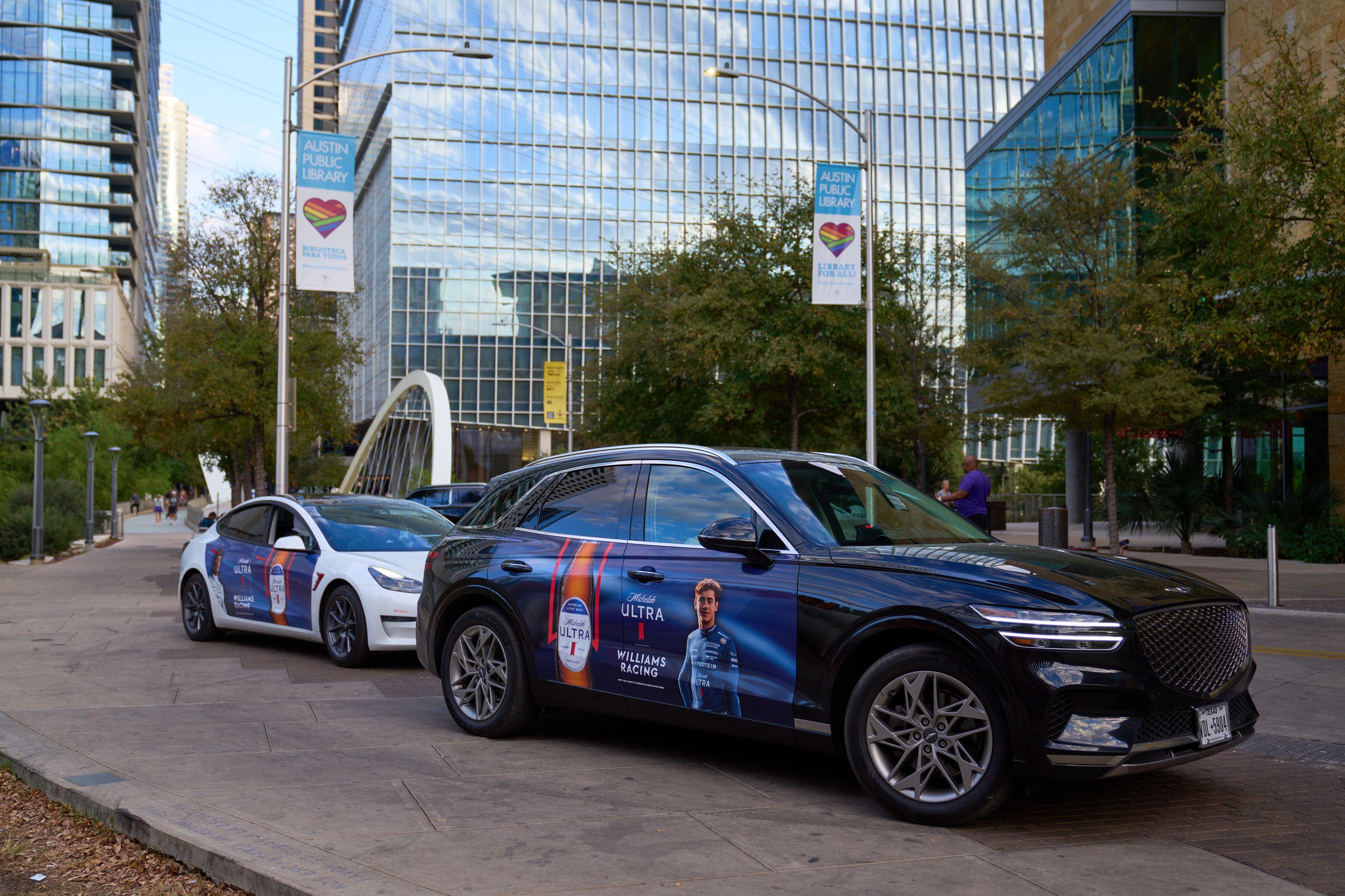 Dark car with a rooftop Michelob Ultra digital ad on a downtown Austin street — Downtown Austin photography, Austin A dark car with a rooftop Michelob Ultra digital ad on a downtown Austin street beside a white arched bridge.