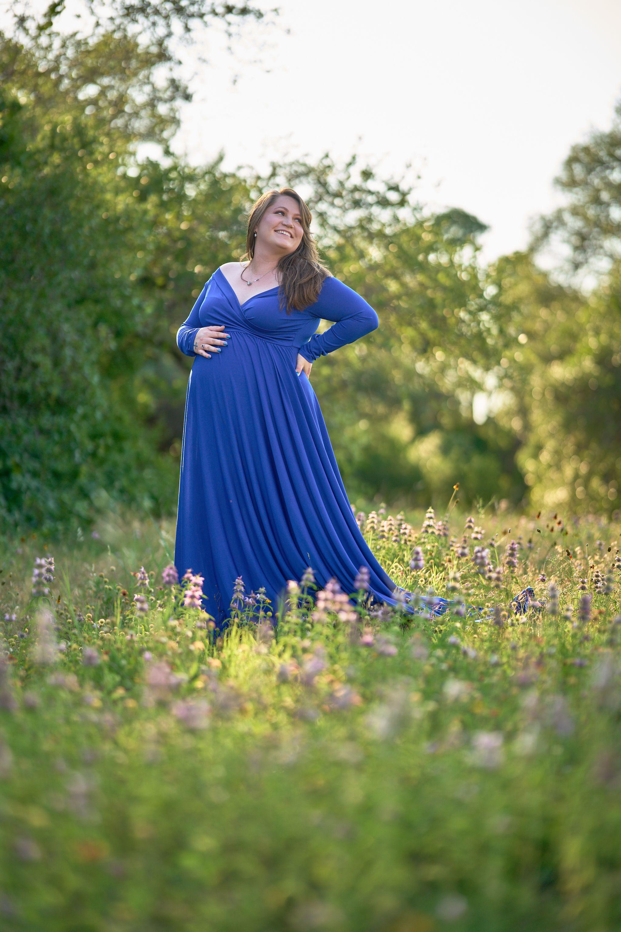 Woman in a blue maternity gown standing in a meadow, hand on her bump — Seasonal Wildflower Season in Texas photography, Austin A woman in a blue maternity gown standing in a meadow, hand on her bump.
