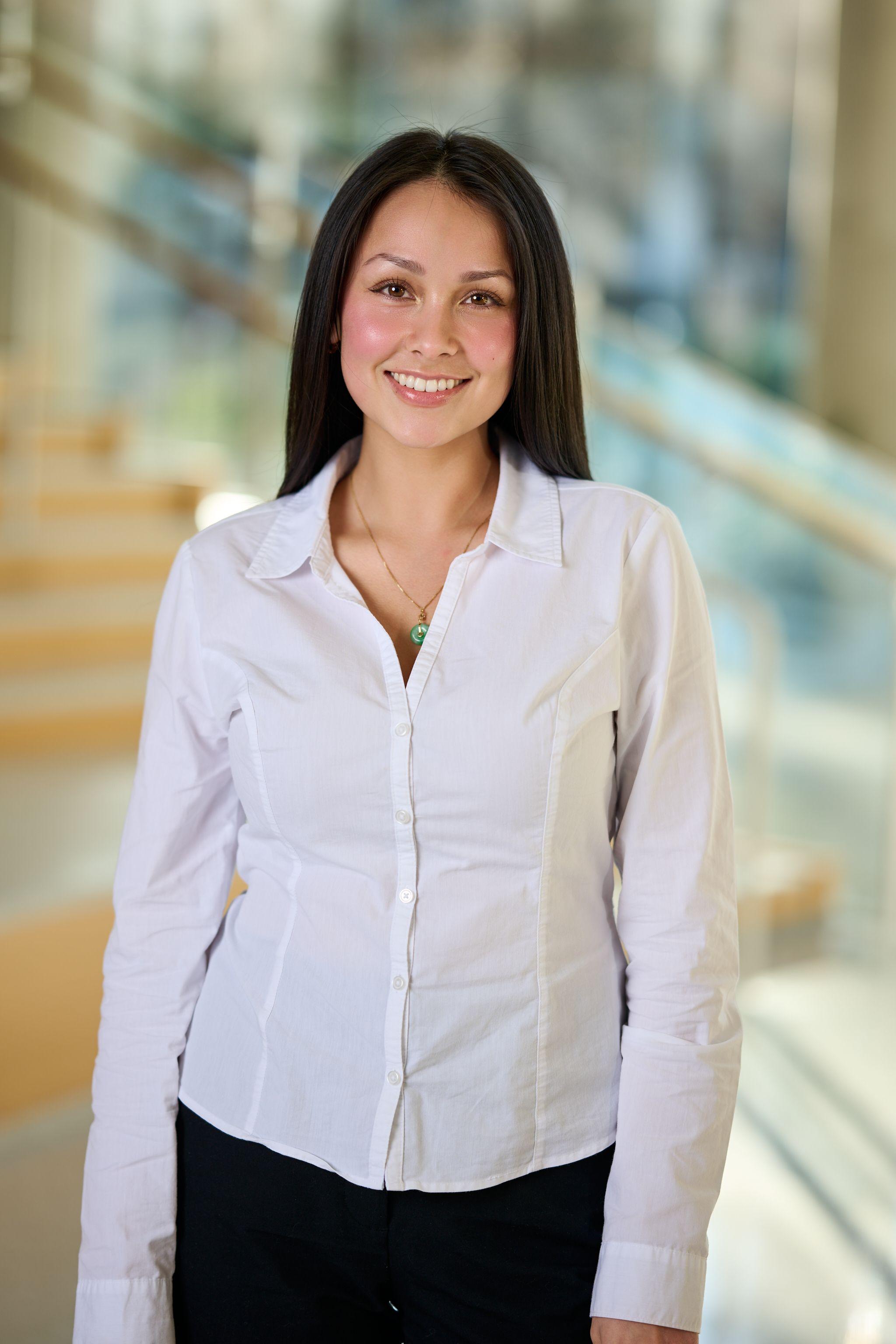 Woman in a white button shirt smiling in an office atrium, a staircase blurred — Business headshots, Austin A woman in a white button shirt smiling in an office atrium, a staircase blurred behind her