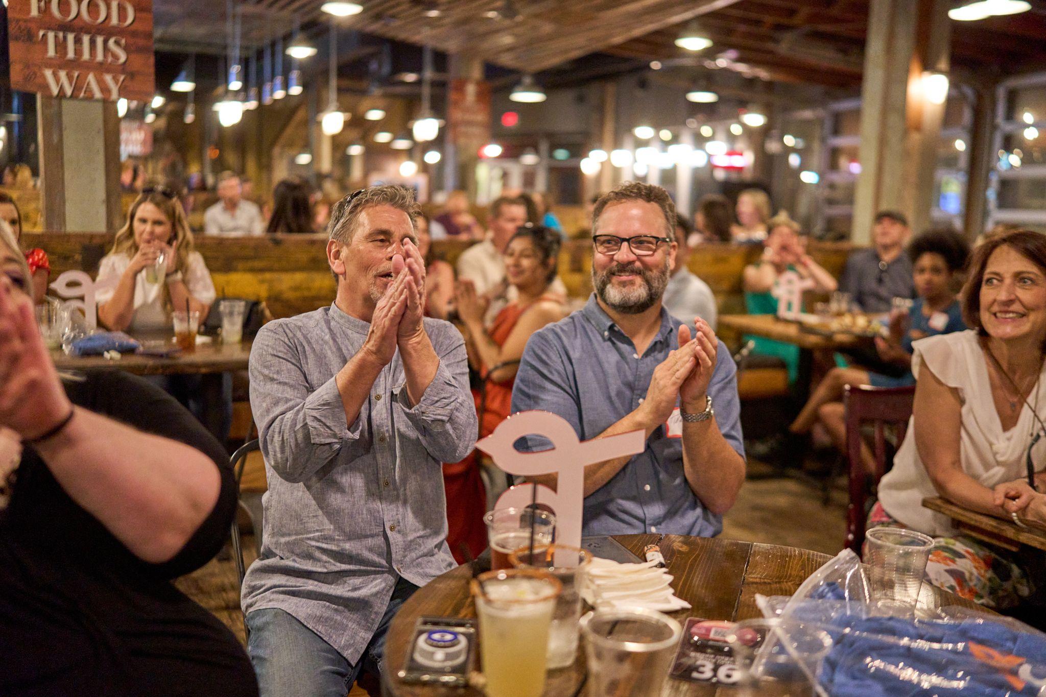 Two men applauding at a long table in a busy restaurant — Team offsite photography, Austin Two men applauding at a long table in a busy restaurant