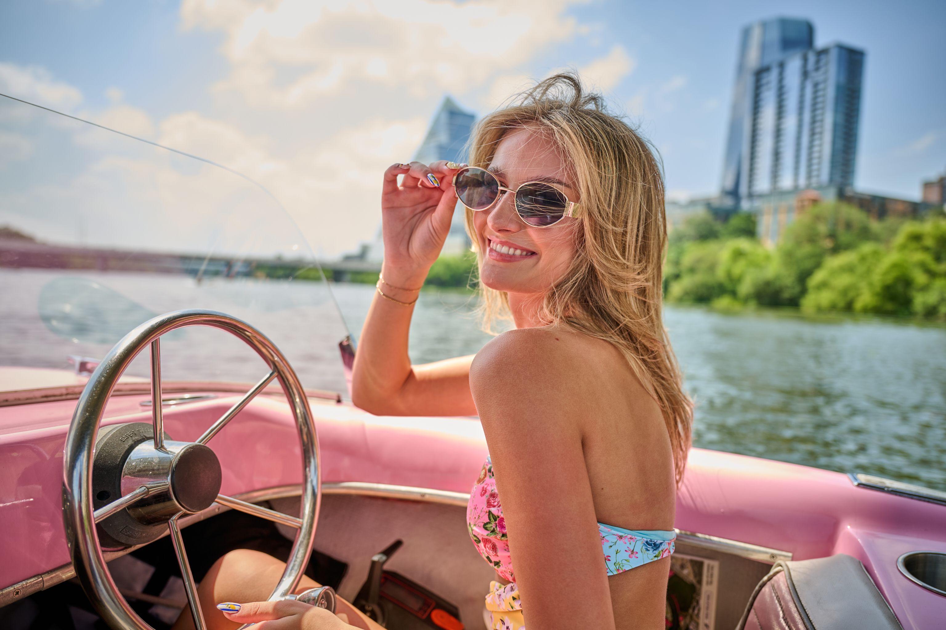 Model at the wheel of a pink vintage boat with the downtown Austin skyline — Bachelor & Bachelorette photography, Austin A model at the wheel of a pink vintage boat with the downtown Austin skyline behind her.