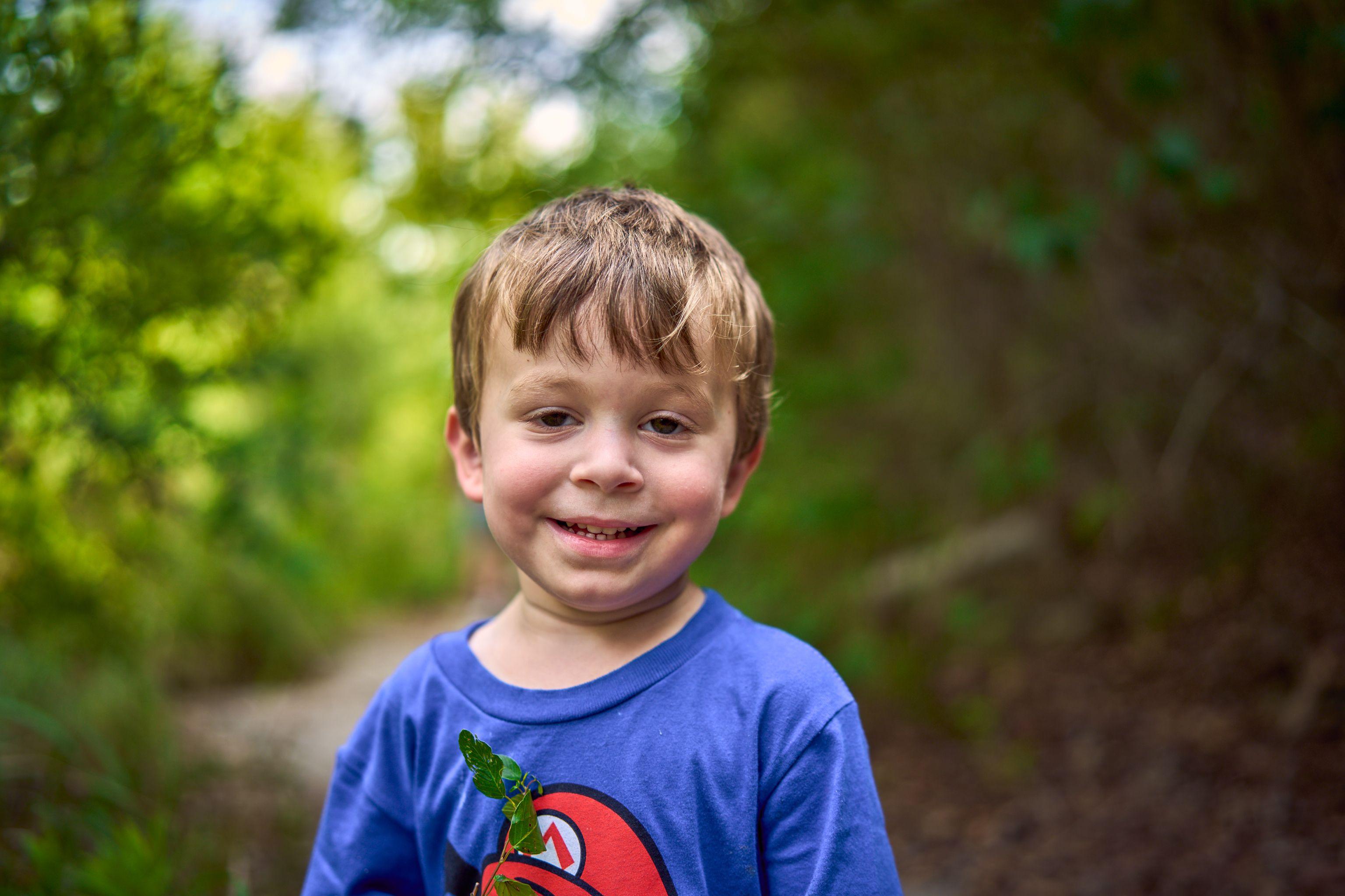 Boy in a blue Mario T-shirt smiling in dappled green light — Bull Creek District Park photography, Austin A boy in a blue Mario T-shirt smiling in dappled green light.