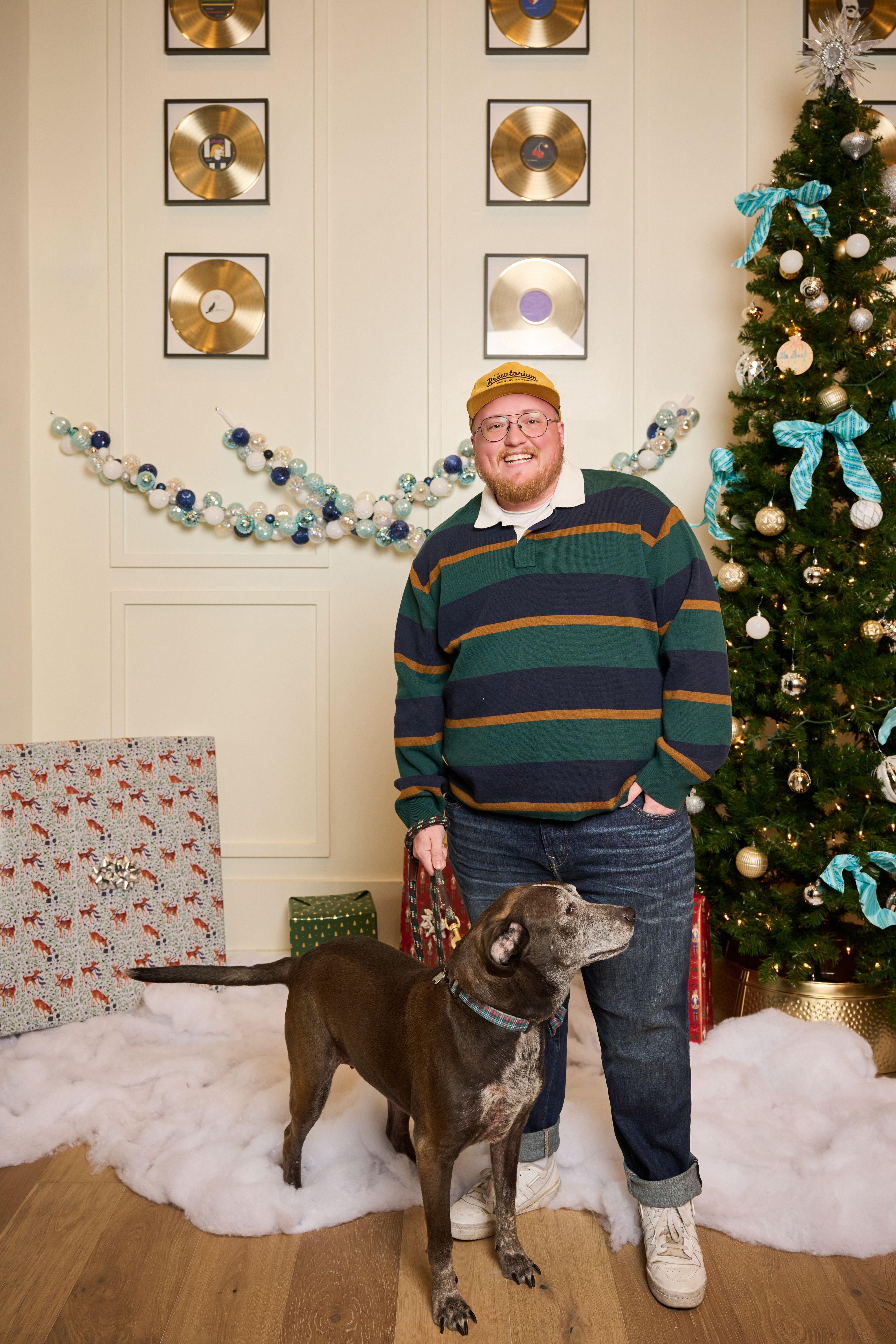 Man in a striped rugby shirt standing with his gray dog beside a Christmas tree — Mobile photo studio, Austin A man in a striped rugby shirt standing with his gray dog beside a Christmas tree on a holiday set